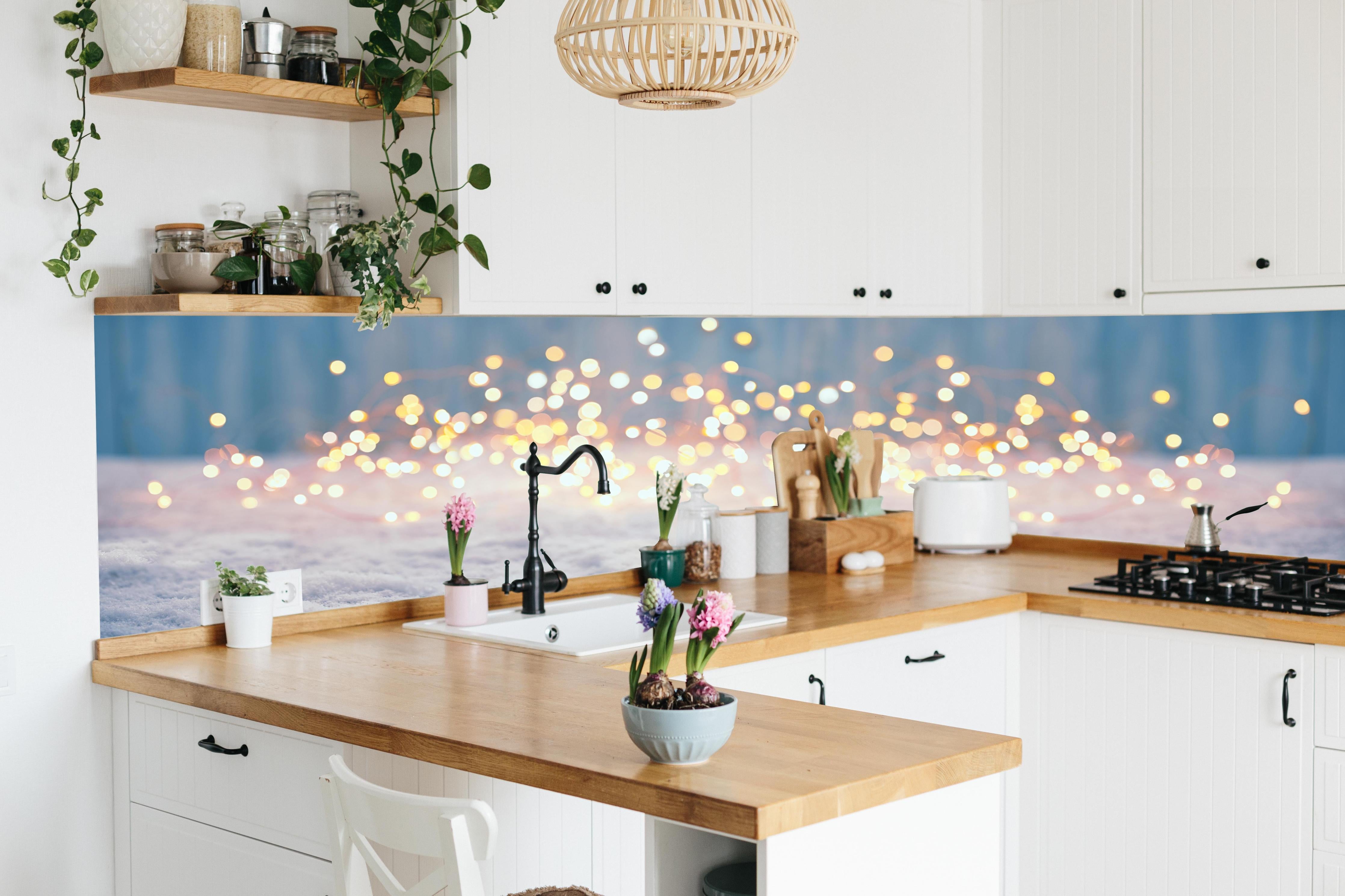 Küche - Magische Winterlandschaft mit goldenem Bokeh hinter weißen Hochglanz-Küchenregalen und schwarzem Wasserhahn