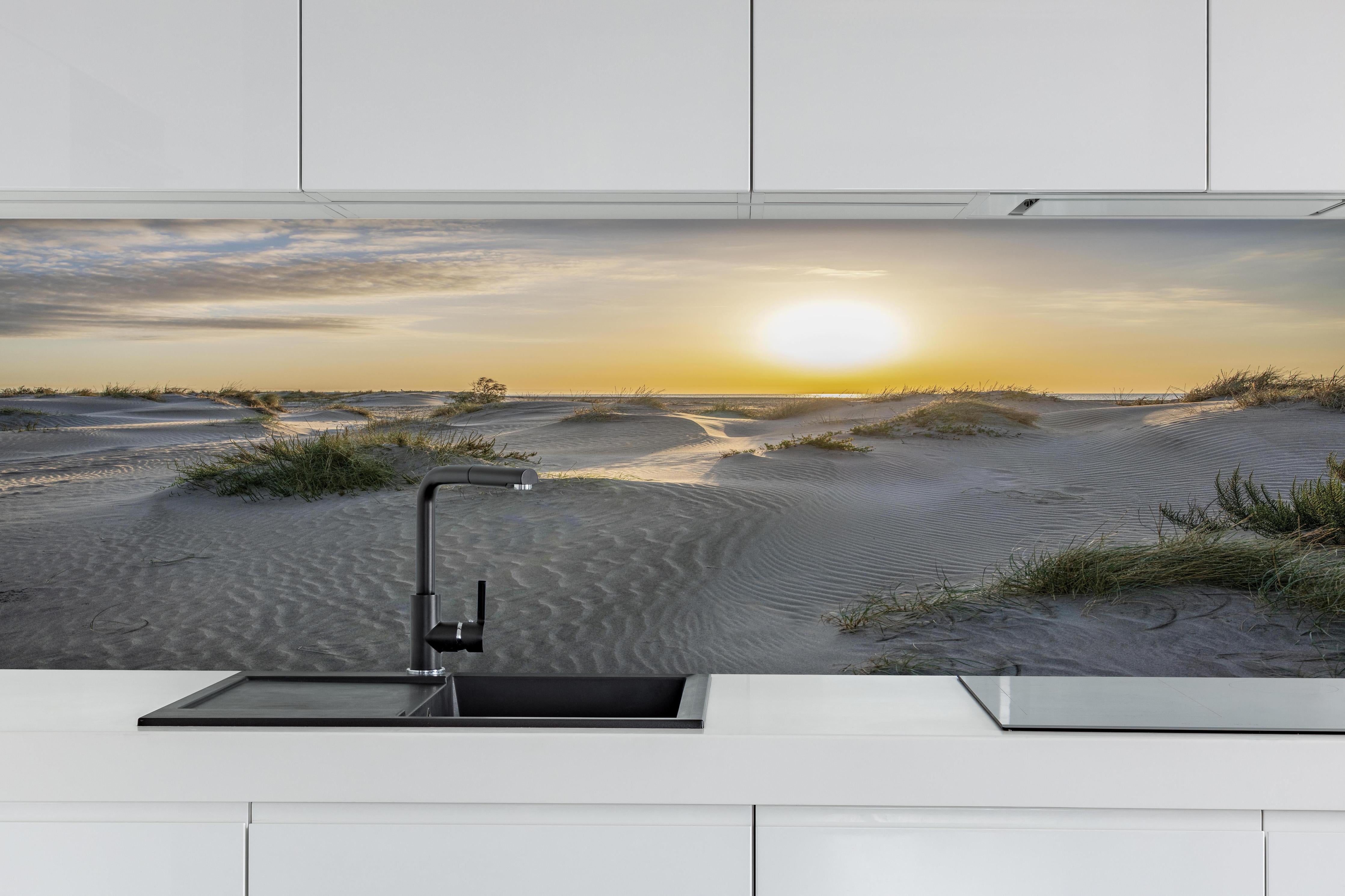 Küche - Malerische Sanddünenlandschaft mit goldenem Sonnenuntergang am Meer hinter weißen Hochglanz-Küchenregalen und schwarzem Wasserhahn
