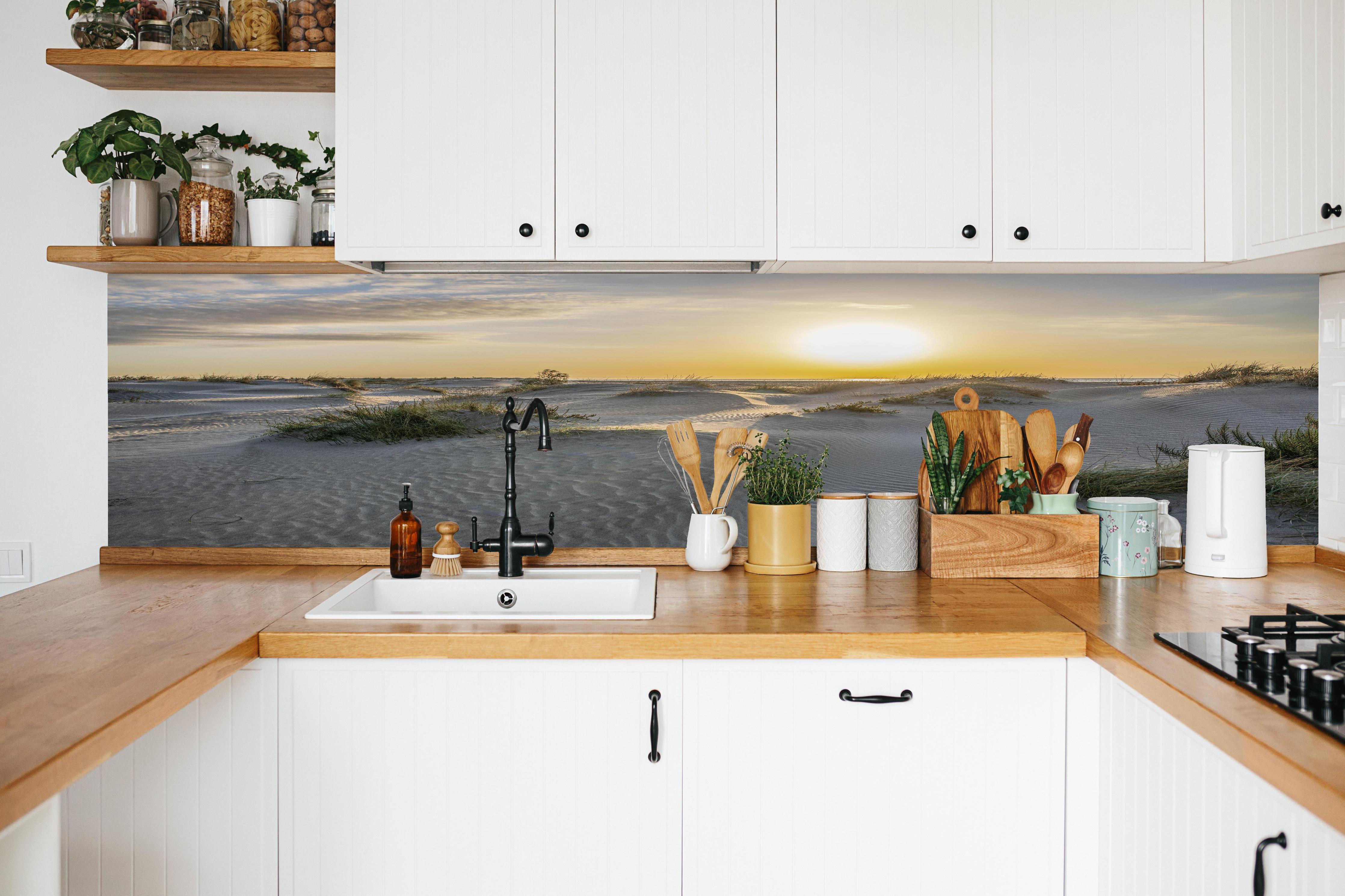 Küche - Malerische Sanddünenlandschaft mit goldenem Sonnenuntergang am Meer hinter weißen Hochglanz-Küchenregalen und schwarzem Wasserhahn