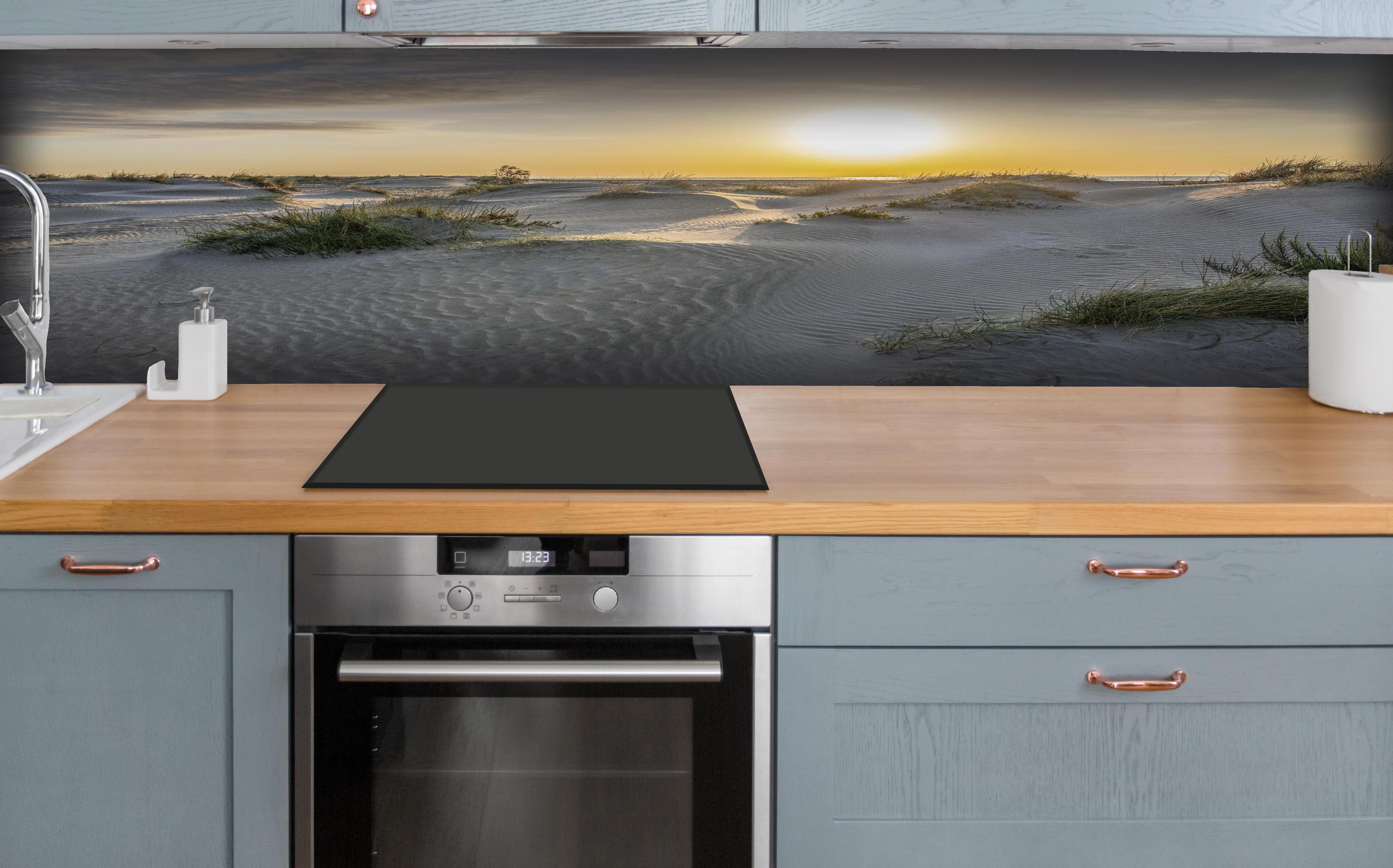 Küche - Malerische Sanddünenlandschaft mit goldenem Sonnenuntergang am Meer hinter weißen Hochglanz-Küchenregalen und schwarzem Wasserhahn