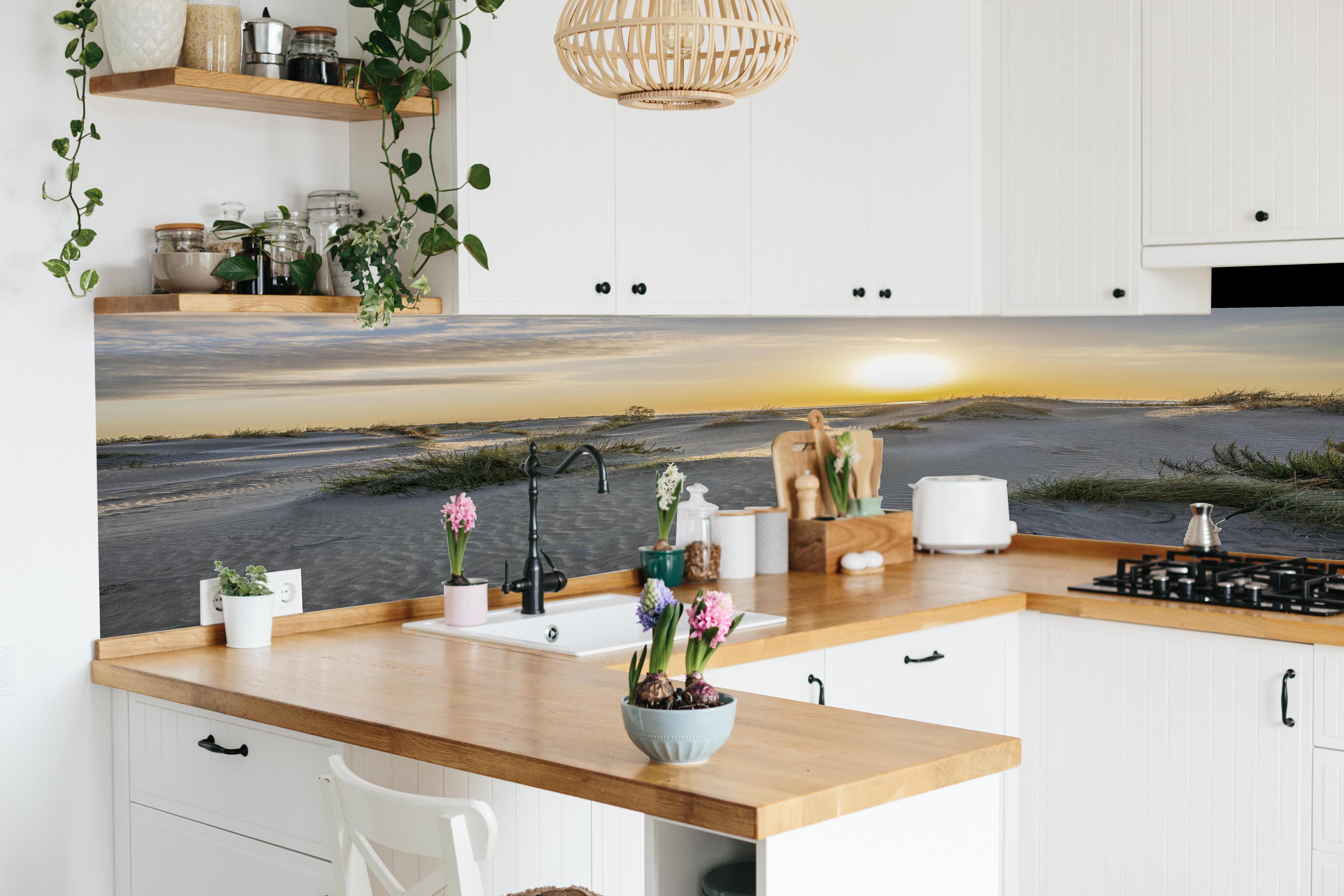 Küche - Malerische Sanddünenlandschaft mit goldenem Sonnenuntergang am Meer hinter weißen Hochglanz-Küchenregalen und schwarzem Wasserhahn