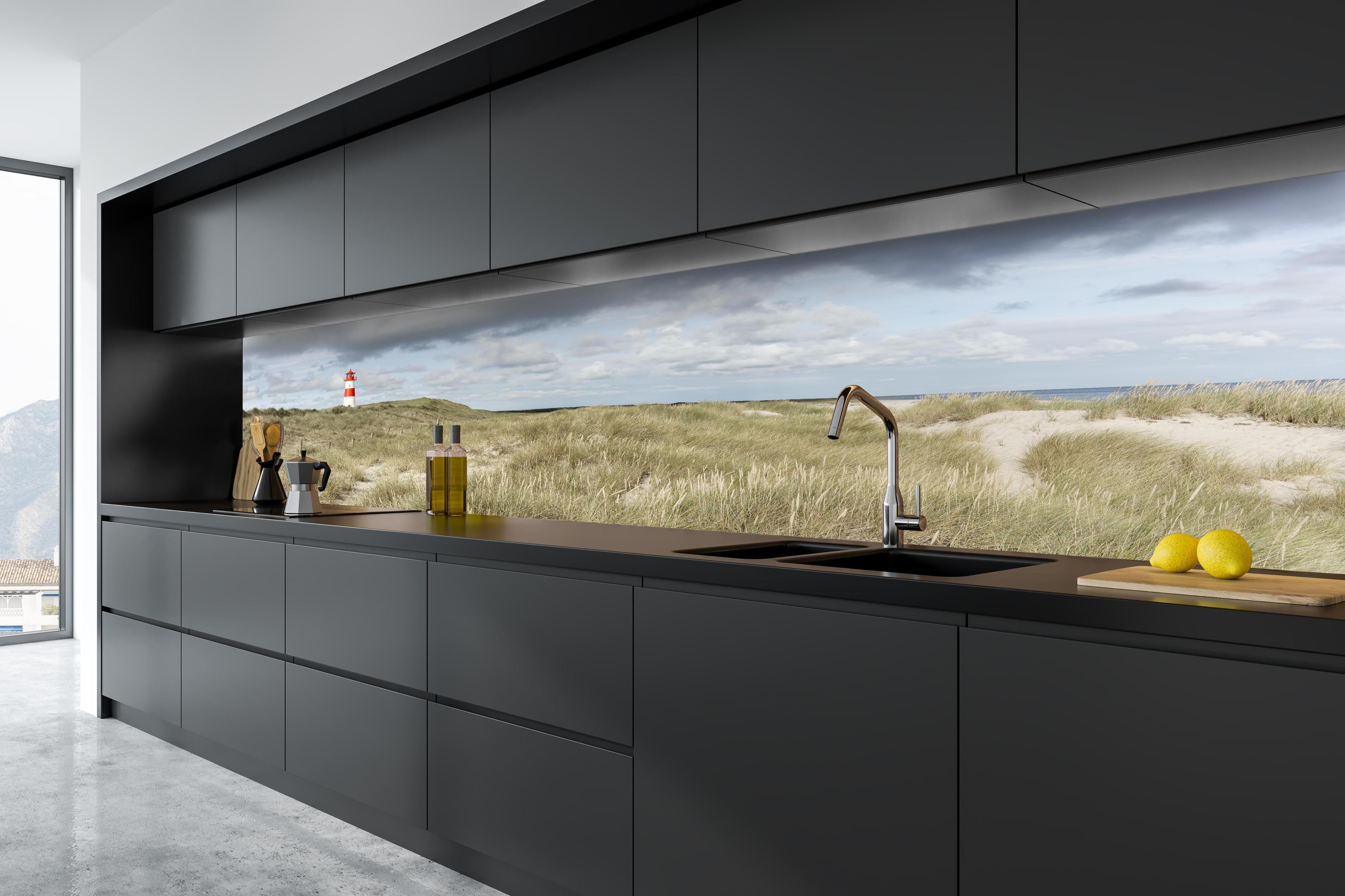 Küche - Malerischer Leuchtturm in den Dünen einer Küstenlandschaft hinter weißen Hochglanz-Küchenregalen und schwarzem Wasserhahn