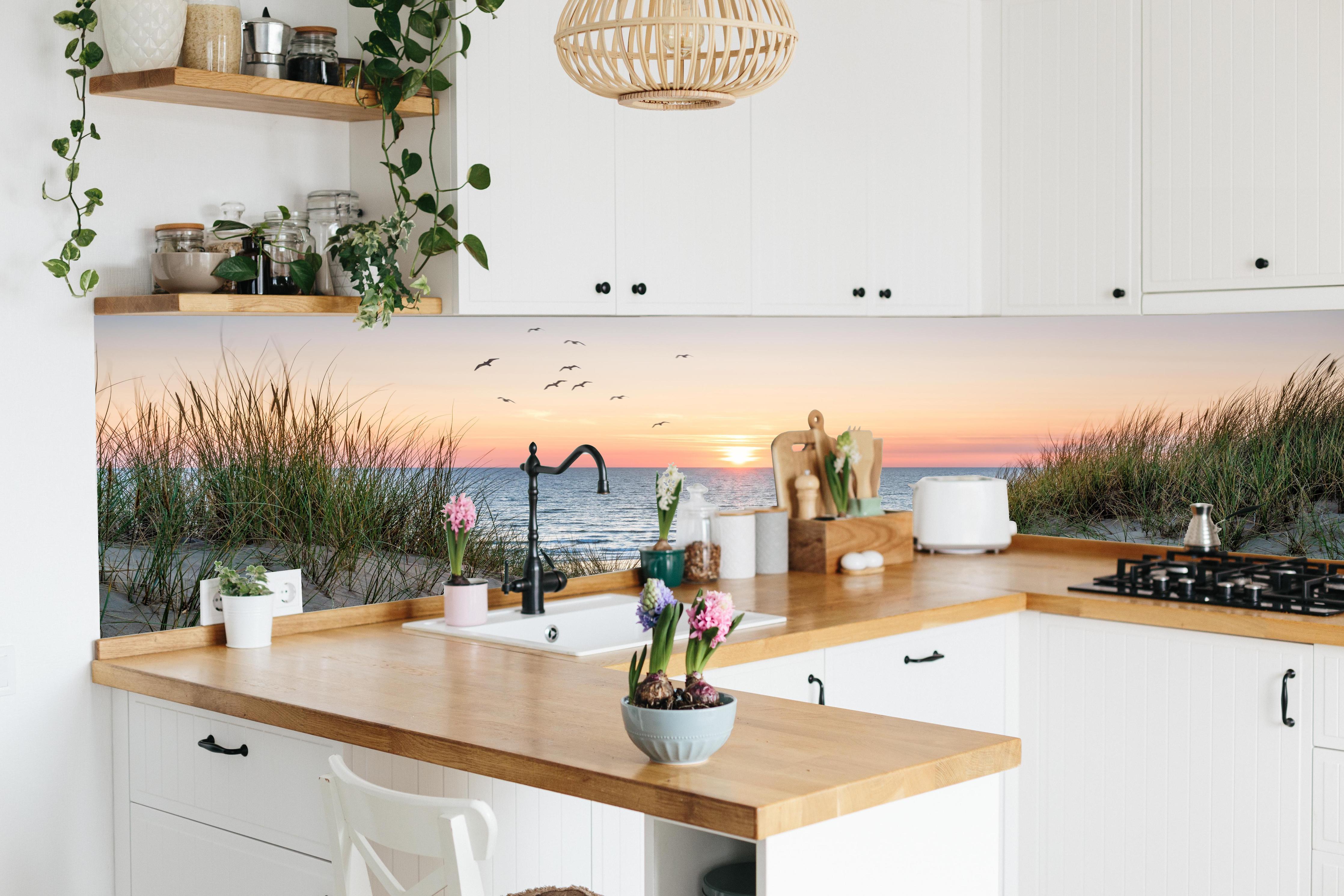 Küche - Malerischer Sonnenuntergang am Dünenstrand hinter weißen Hochglanz-Küchenregalen und schwarzem Wasserhahn