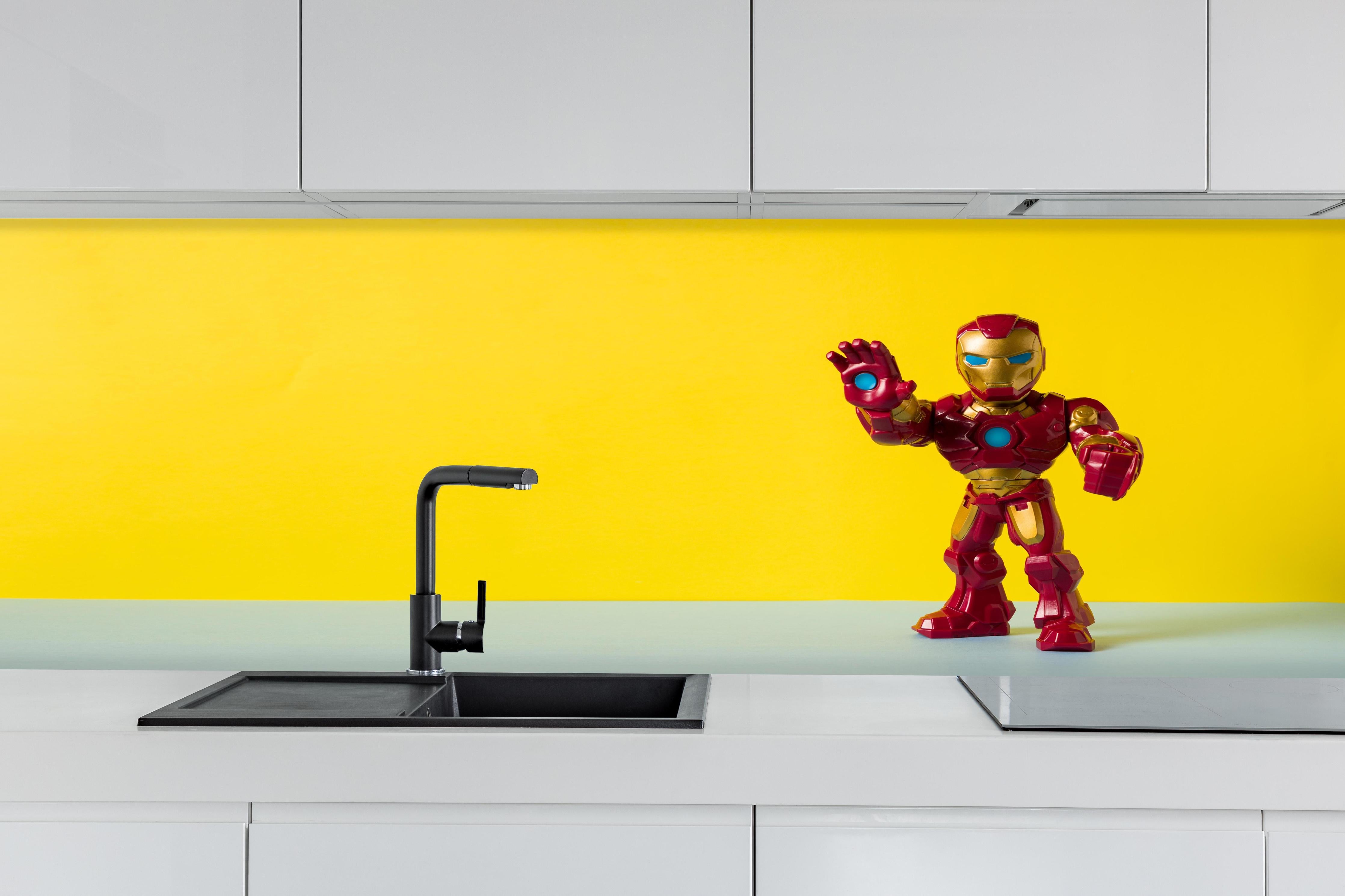 Küche - Marvel Iron Man Sammelfigur auf Gelb hinter weißen Hochglanz-Küchenregalen und schwarzem Wasserhahn