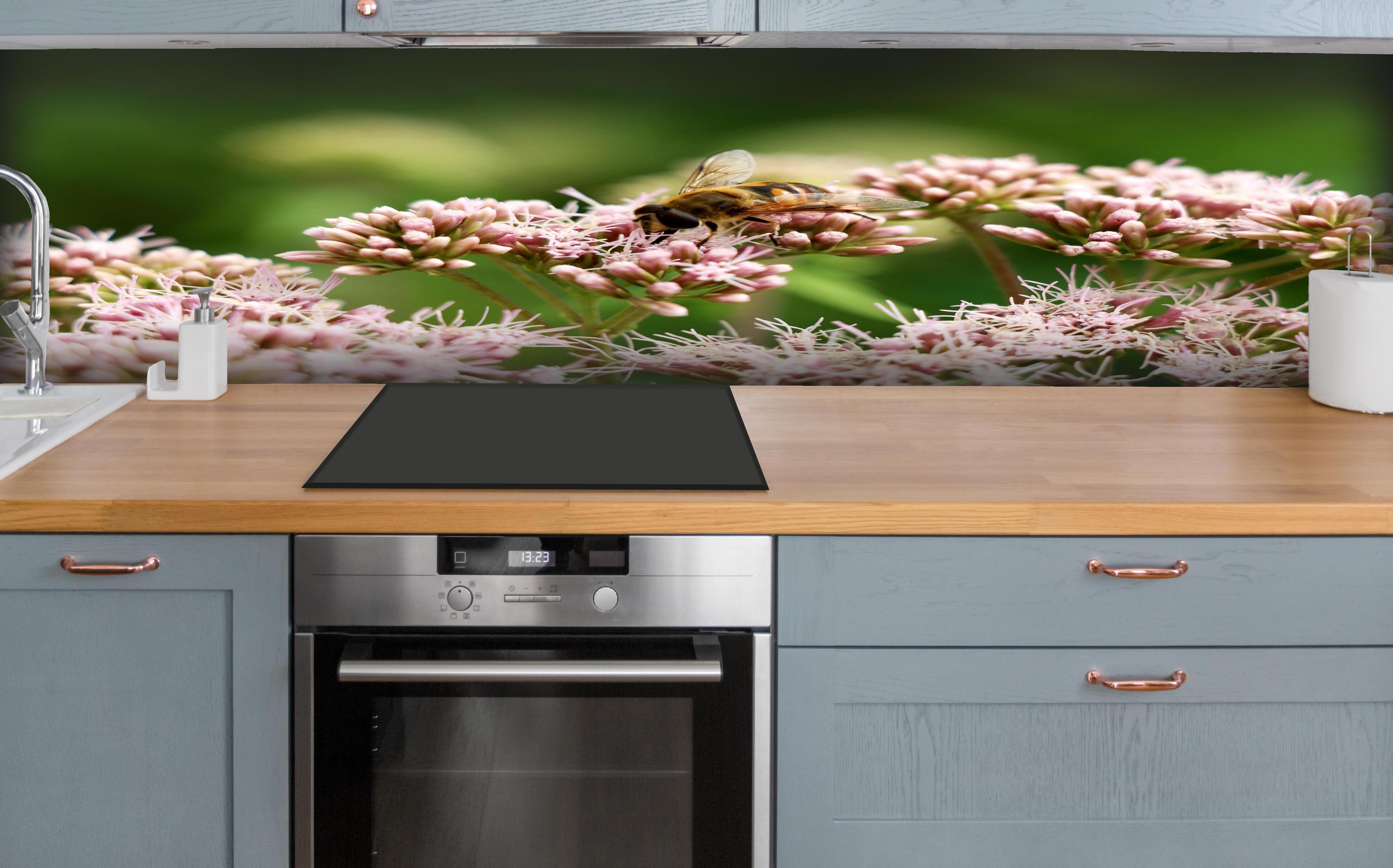 Küche - Nahaufnahme Biene Rosa Blütenpracht hinter weißen Hochglanz-Küchenregalen und schwarzem Wasserhahn