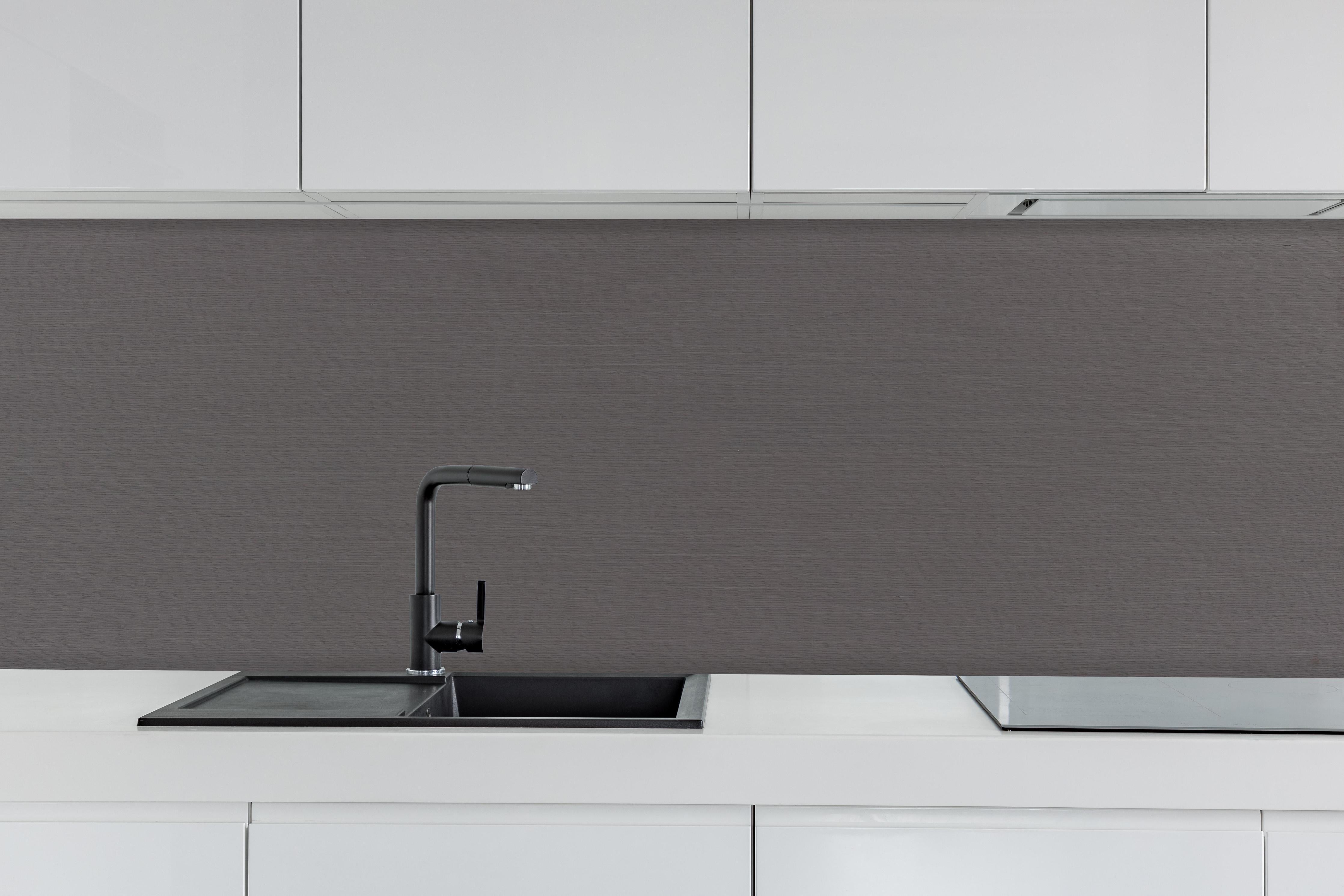 Küche - Nahaufnahme einer grauen, strukturierten Oberfläche mit feinen Fasern
hinter weißen Hochglanz-Küchenregalen und schwarzem Wasserhahn
