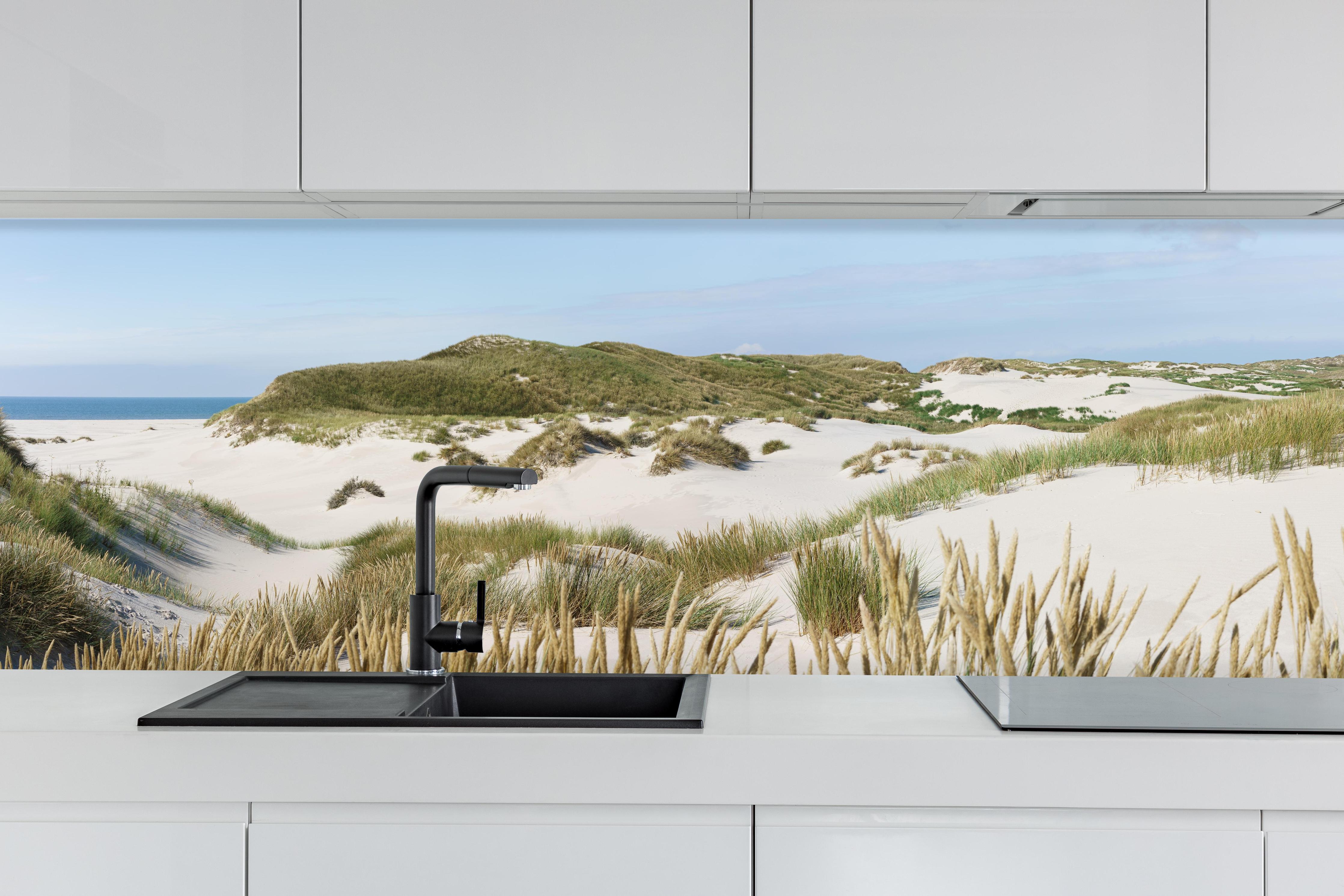 Küche - Naturbelassene Sanddünen mit grasbewachsenen Hügeln und Meerblick hinter weißen Hochglanz-Küchenregalen und schwarzem Wasserhahn