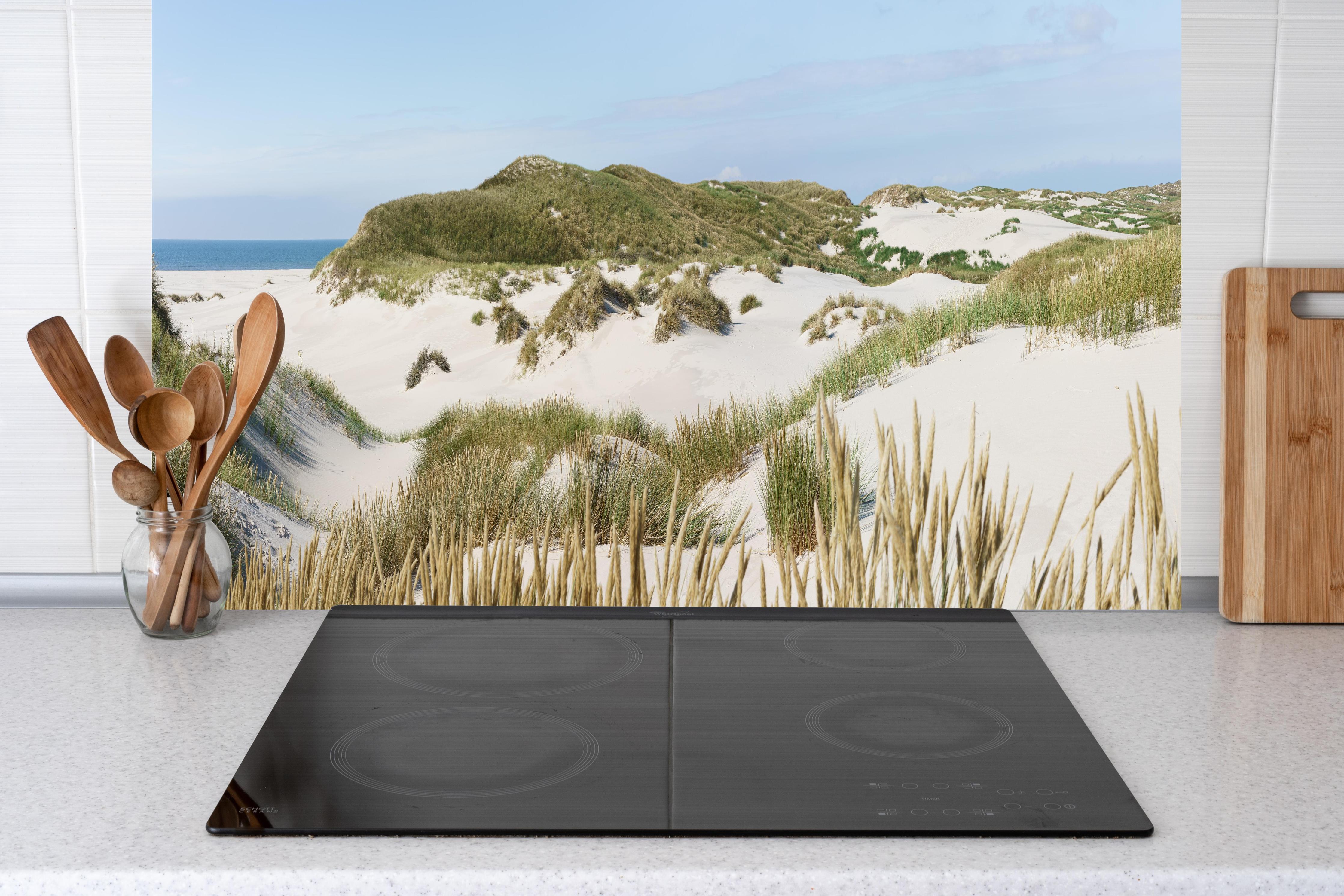 Küche - Naturbelassene Sanddünen mit grasbewachsenen Hügeln und Meerblick hinter weißen Hochglanz-Küchenregalen und schwarzem Wasserhahn