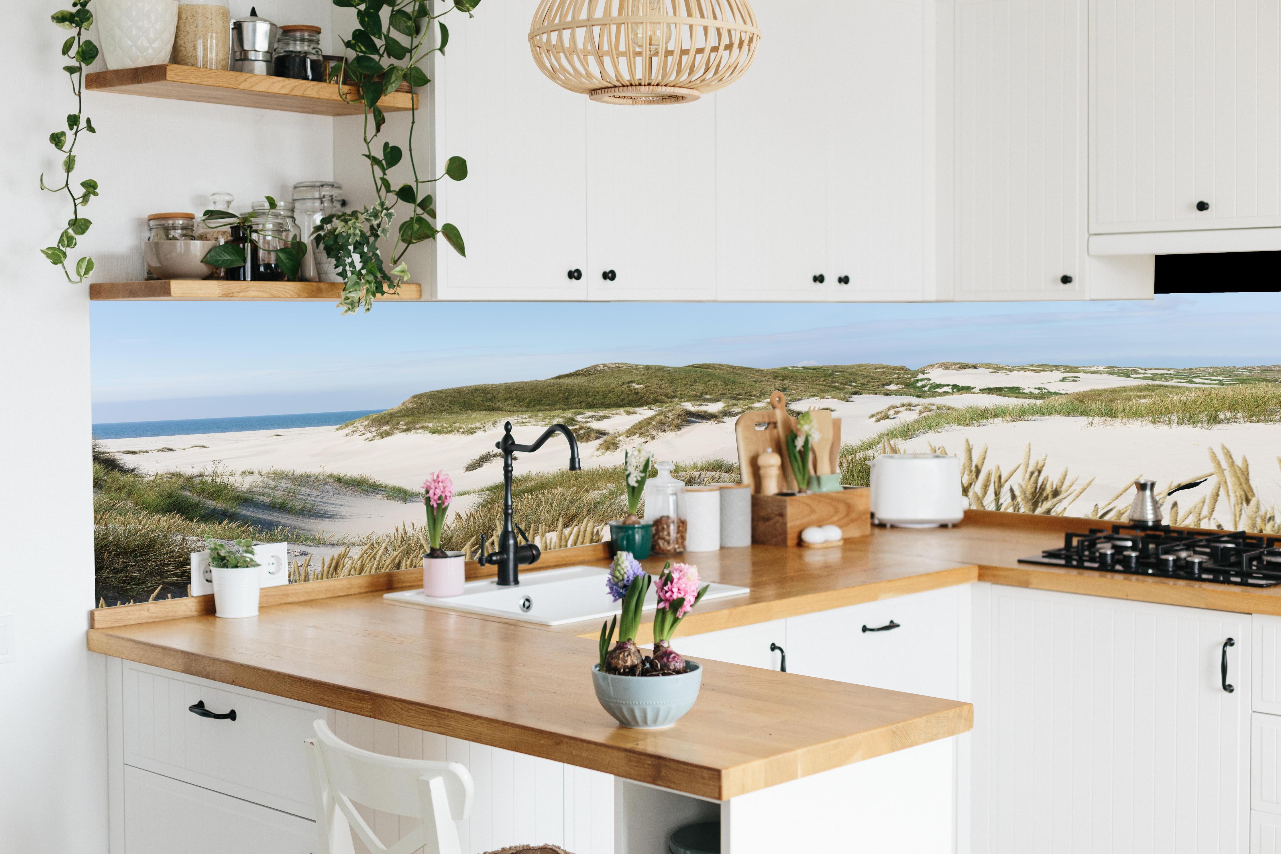 Küche - Naturbelassene Sanddünen mit grasbewachsenen Hügeln und Meerblick hinter weißen Hochglanz-Küchenregalen und schwarzem Wasserhahn