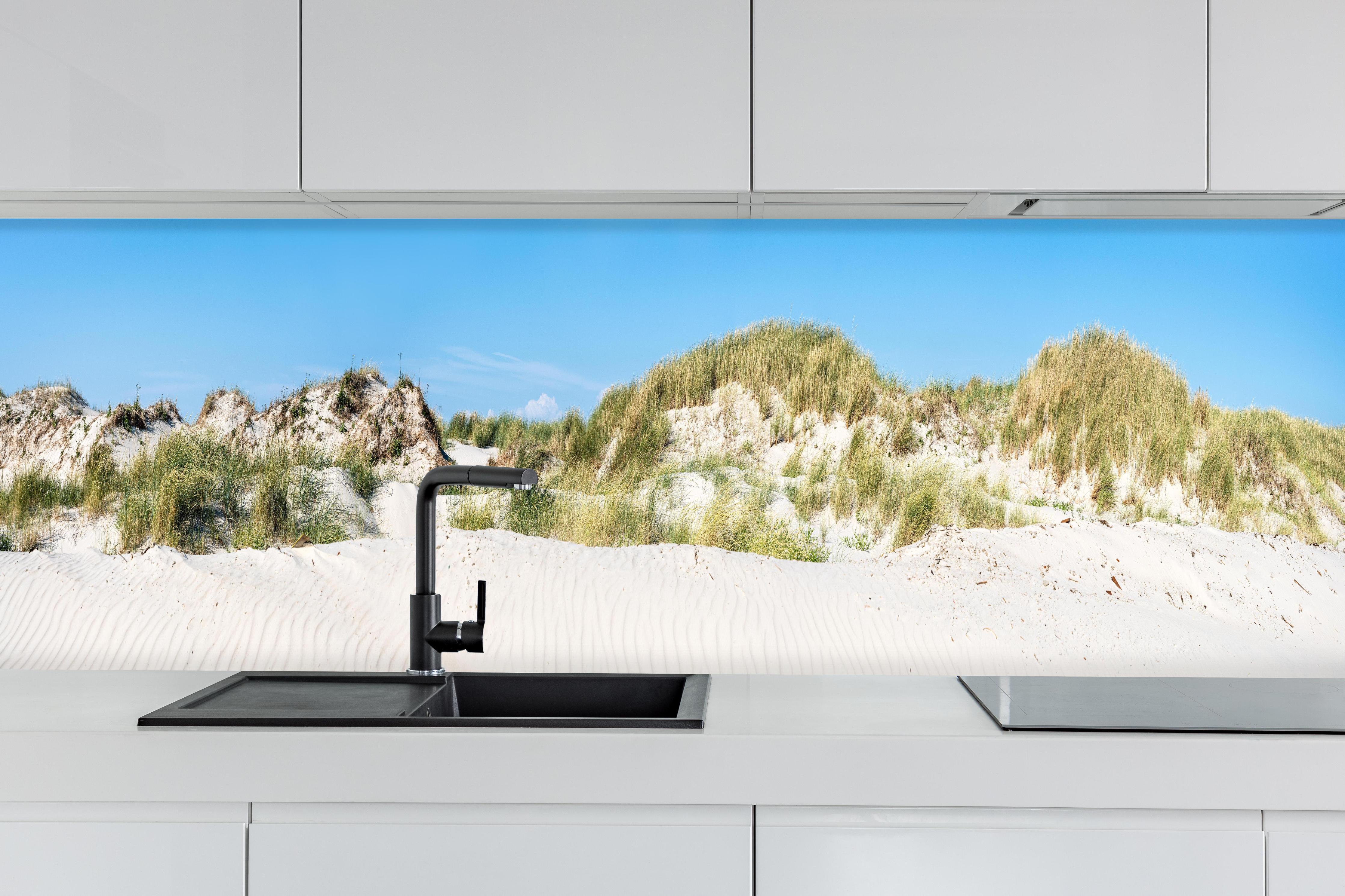 Küche - Panoramaansicht einer traumhaften Dünenlandschaft unter klarem blauen Himmel hinter weißen Hochglanz-Küchenregalen und schwarzem Wasserhahn