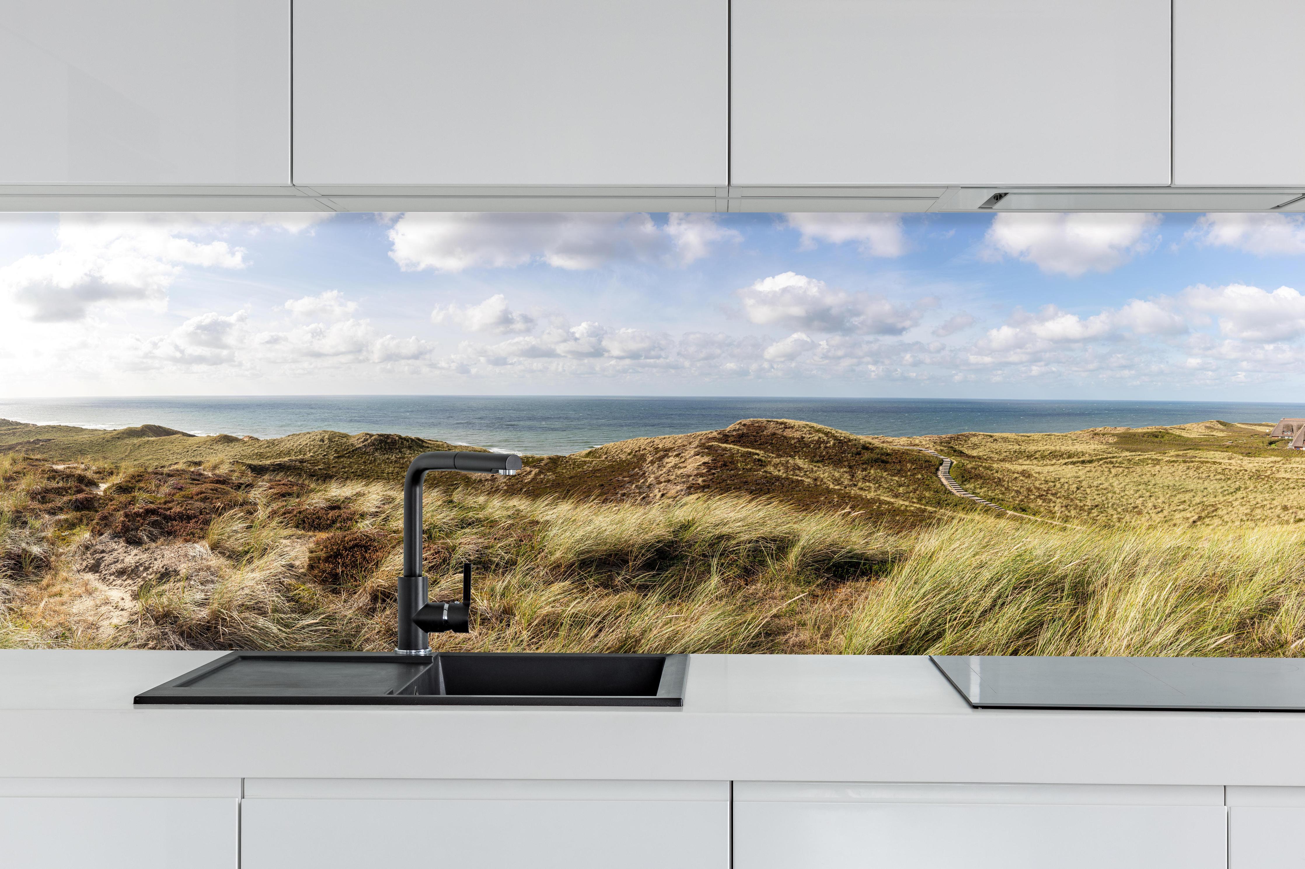 Küche - Panoramaaussicht über sanfte Hügel und die Küste am Meer hinter weißen Hochglanz-Küchenregalen und schwarzem Wasserhahn