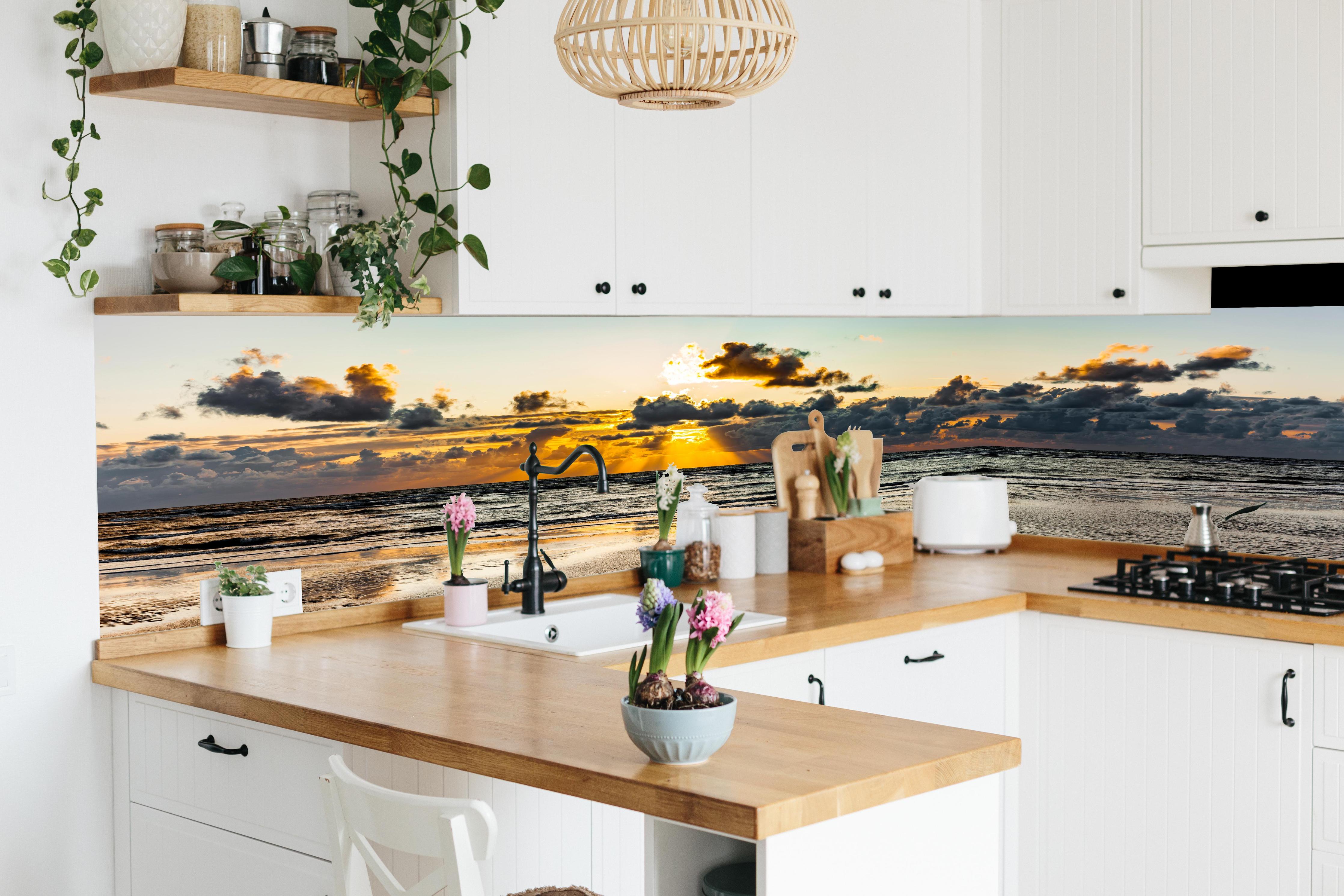 Küche - Panoramablick auf Sonnenuntergang über dem ruhigen Ozean hinter weißen Hochglanz-Küchenregalen und schwarzem Wasserhahn