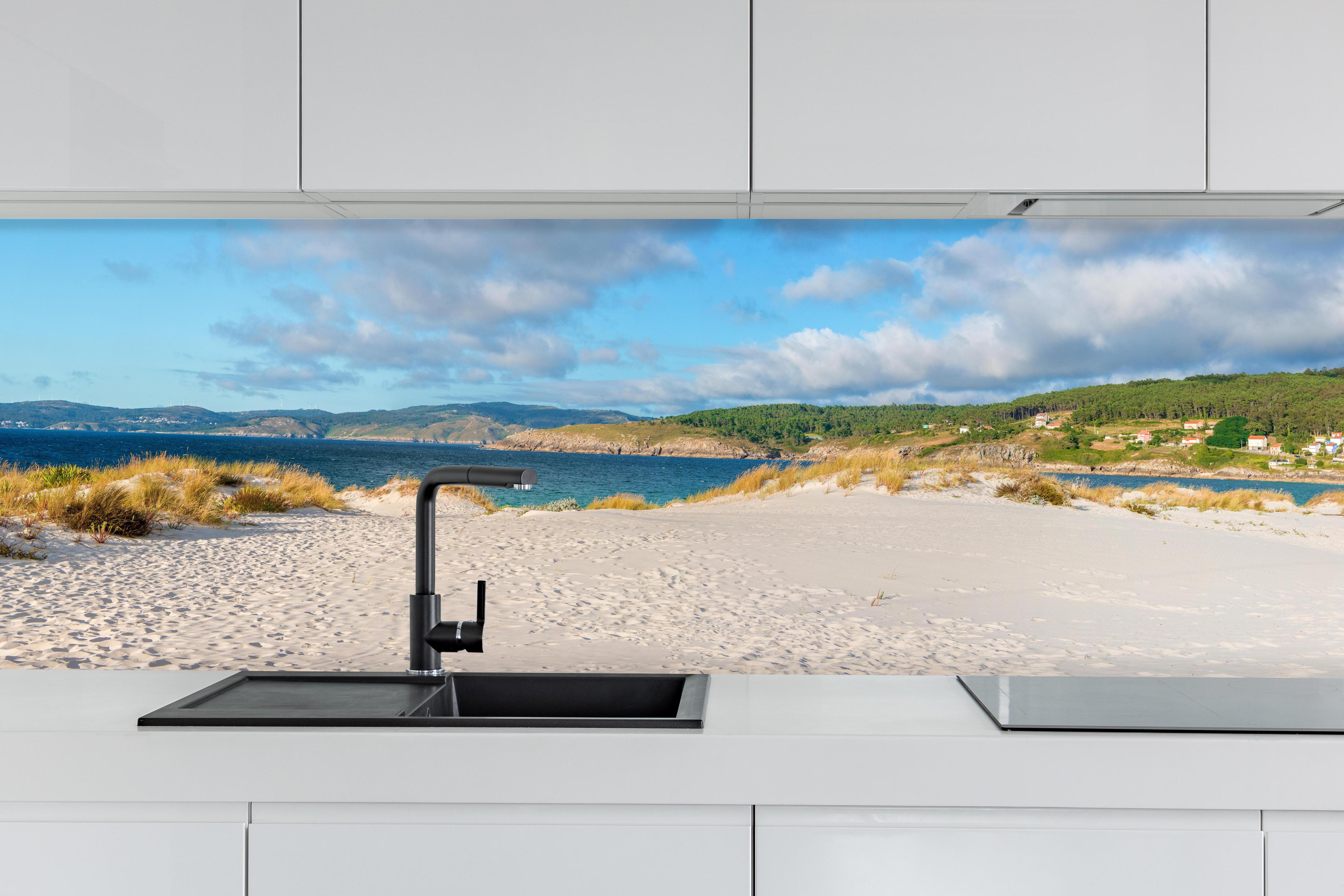 Küche - Panoramablick auf einen traumhaften Strand mit sanften Sanddünen und klarem Wasser hinter weißen Hochglanz-Küchenregalen und schwarzem Wasserhahn