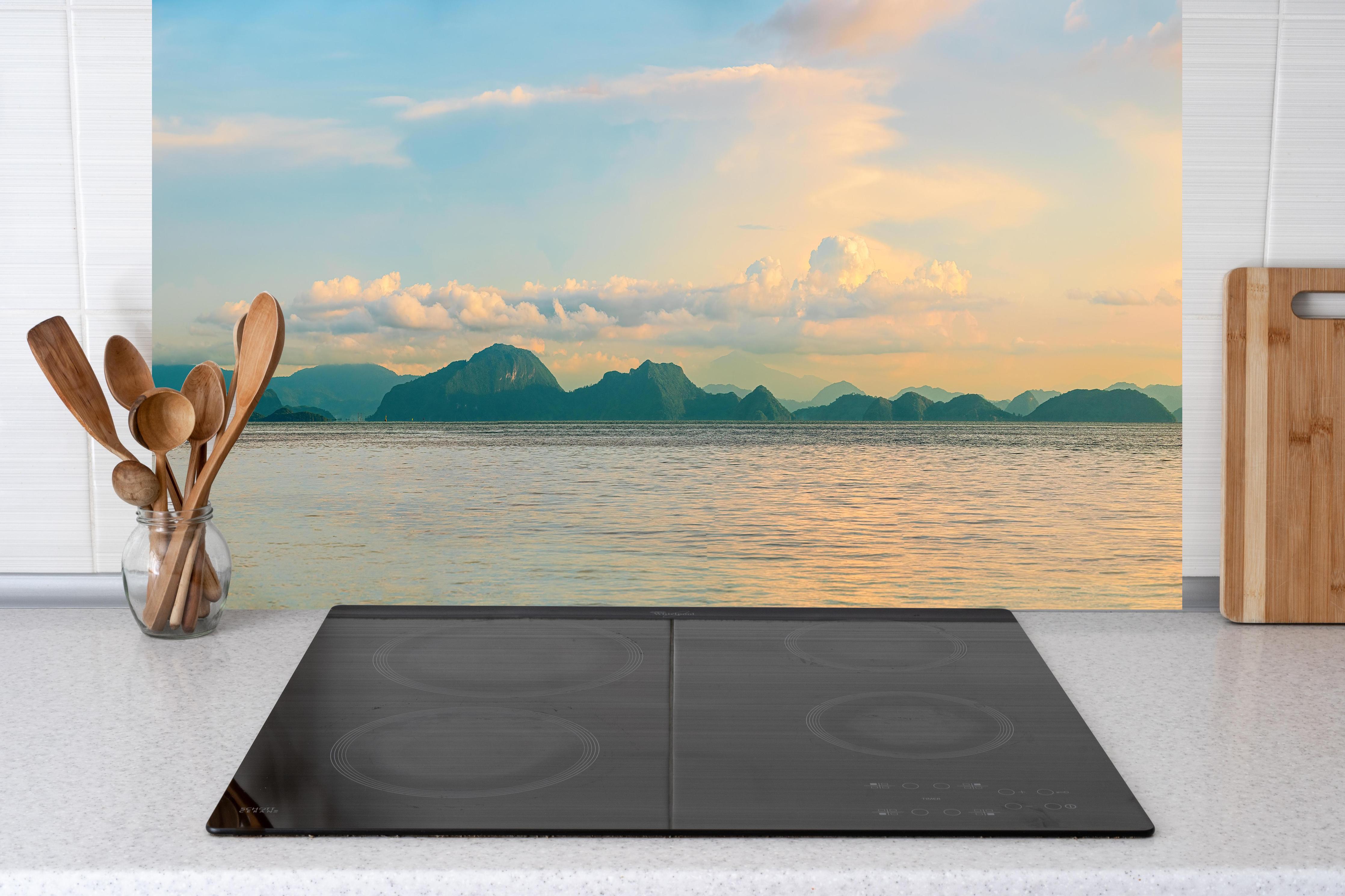 Küche - Panoramablick auf idyllische Küstenlandschaft mit Berge im Hintergrund hinter weißen Hochglanz-Küchenregalen und schwarzem Wasserhahn