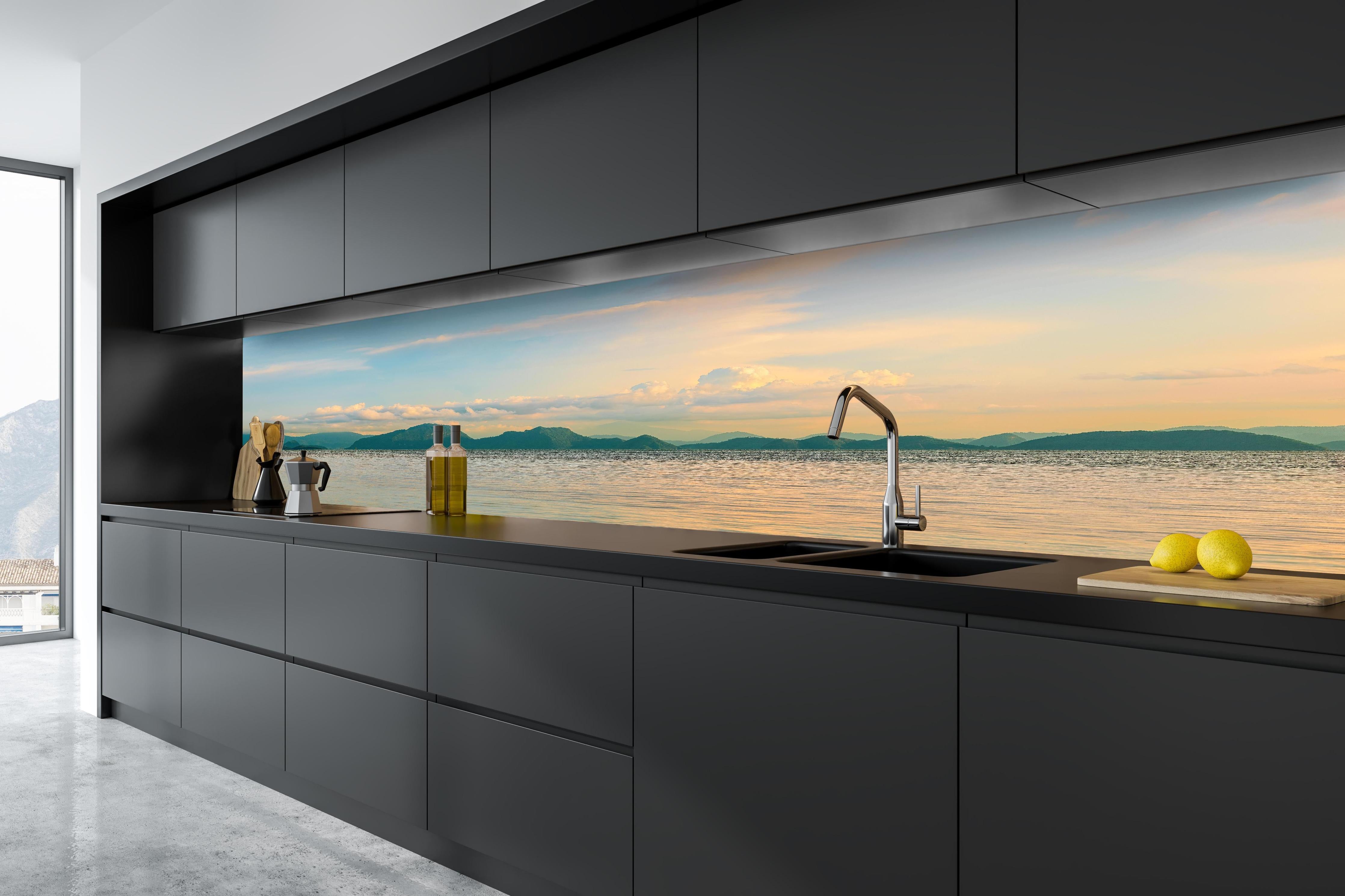 Küche - Panoramablick auf idyllische Küstenlandschaft mit Berge im Hintergrund hinter weißen Hochglanz-Küchenregalen und schwarzem Wasserhahn