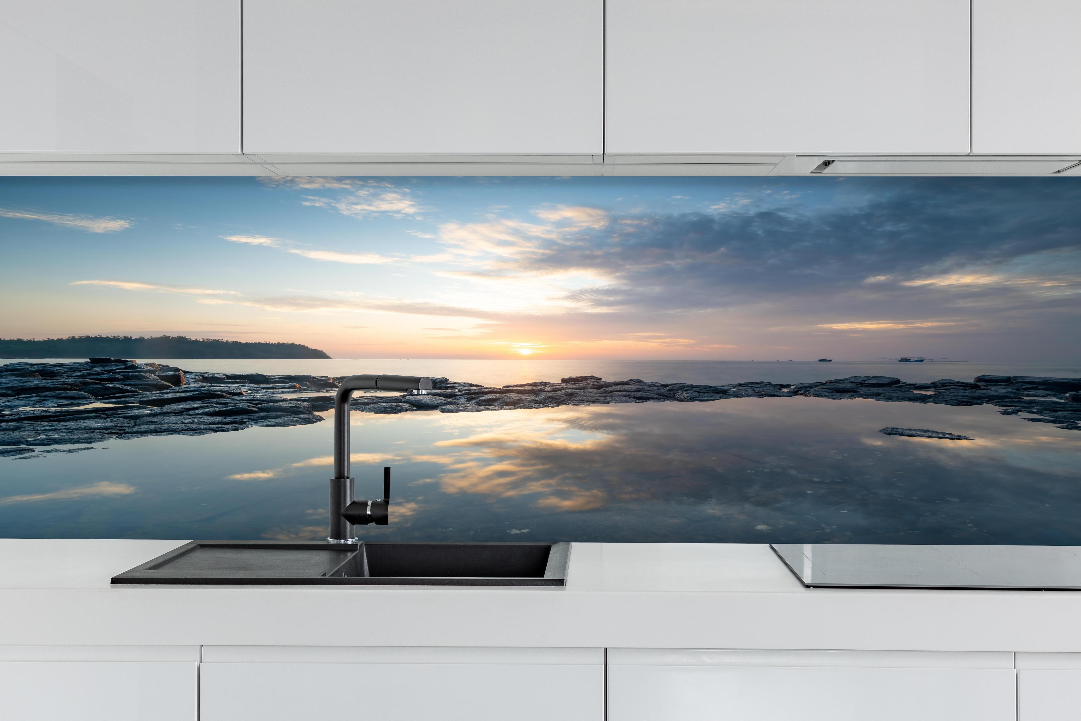 Küche - Pittoresker Sonnenuntergang über dem ruhigen Meer mit reflektierendem Wasser hinter weißen Hochglanz-Küchenregalen und schwarzem Wasserhahn