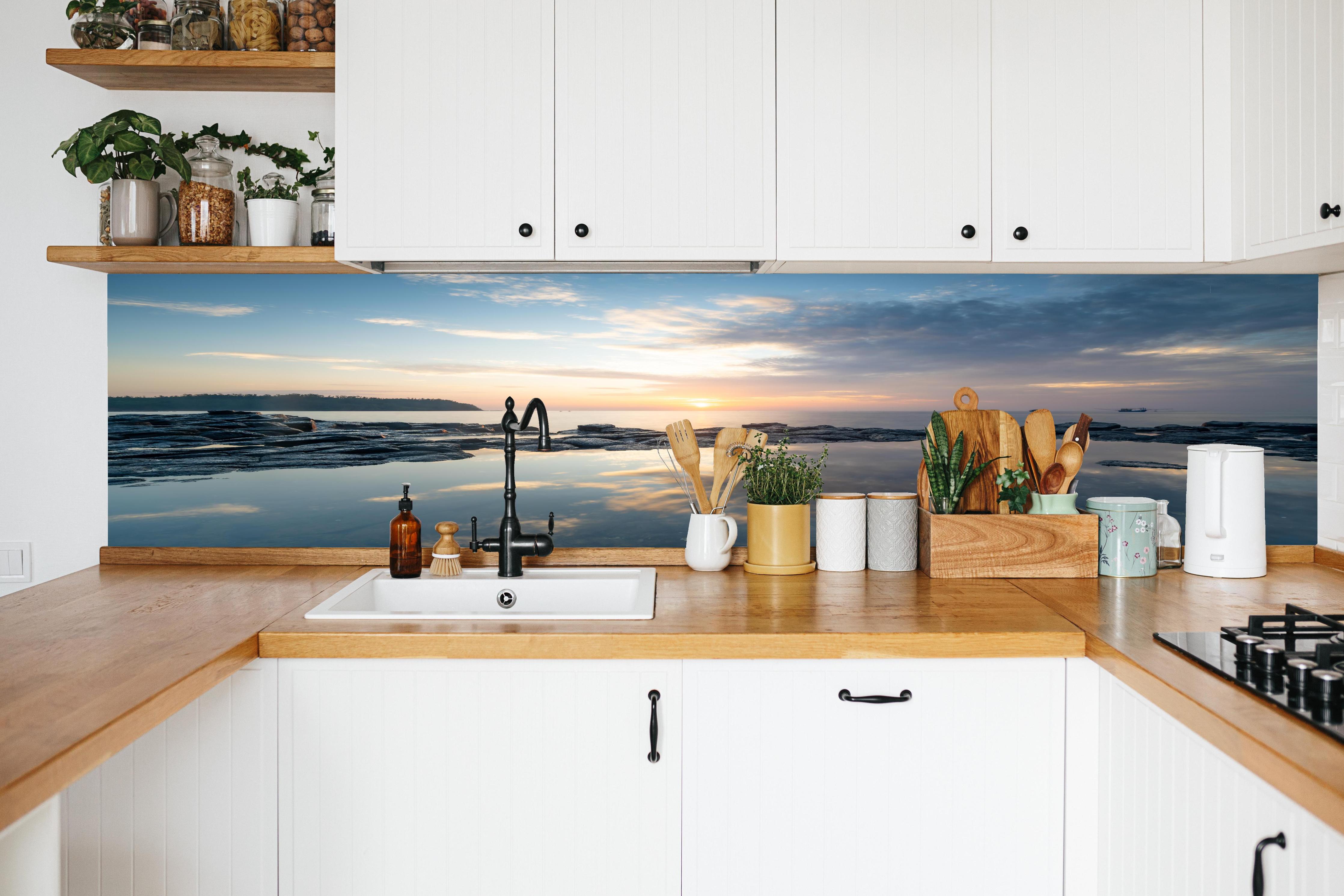 Küche - Pittoresker Sonnenuntergang über dem ruhigen Meer mit reflektierendem Wasser hinter weißen Hochglanz-Küchenregalen und schwarzem Wasserhahn