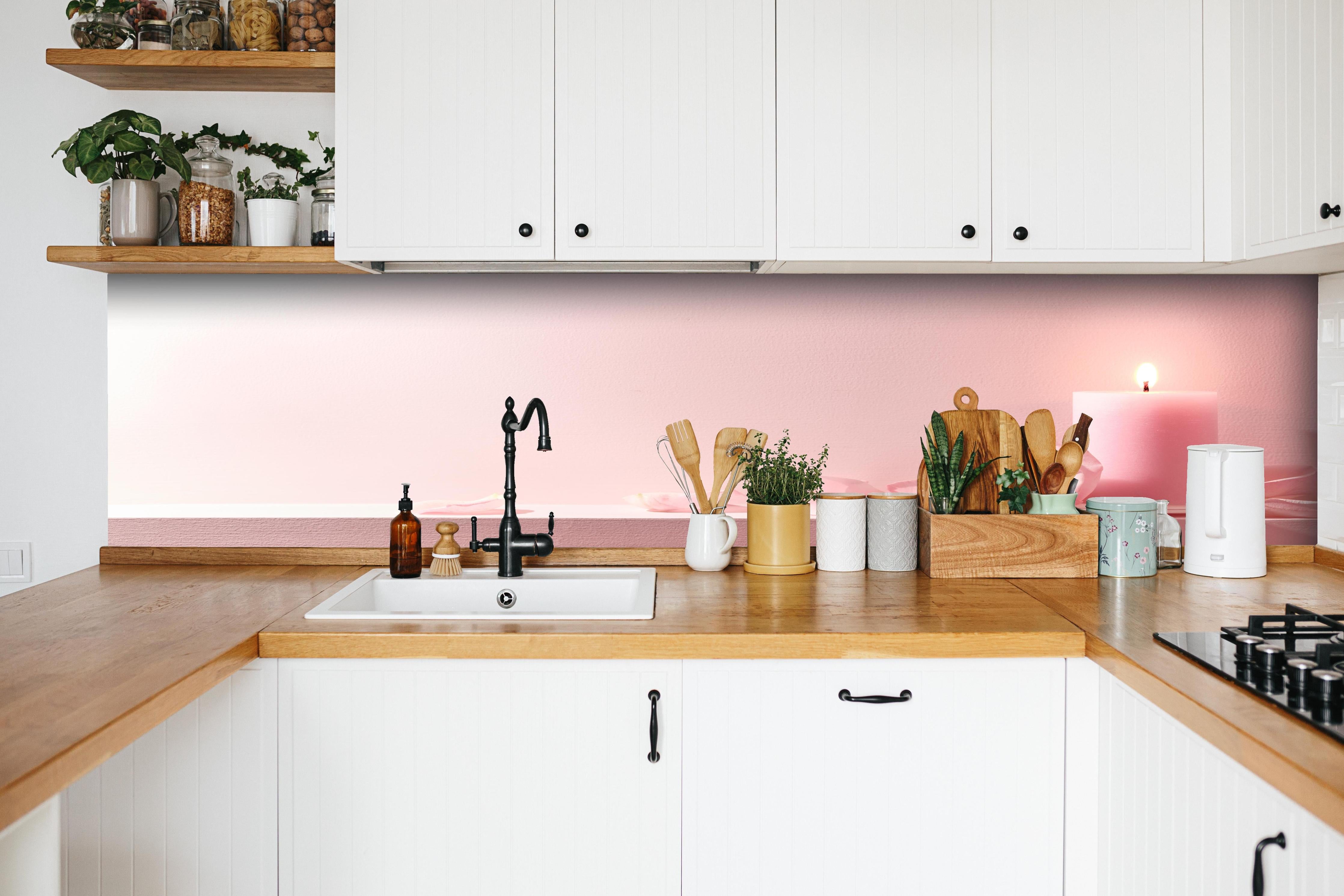 Küche - Rosa Rosen und Kerze auf einem rosa Hintergrund hinter weißen Hochglanz-Küchenregalen und schwarzem Wasserhahn