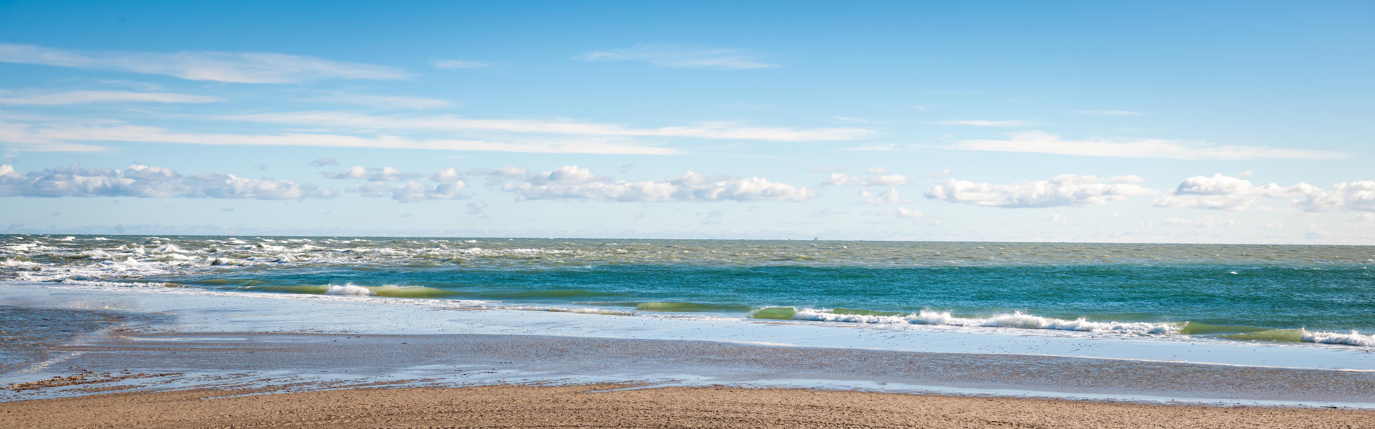 Küchenrückwand-Ruhige Küstenlandschaft unter blauem Himmel mit sanften Wellen und feinem Sand