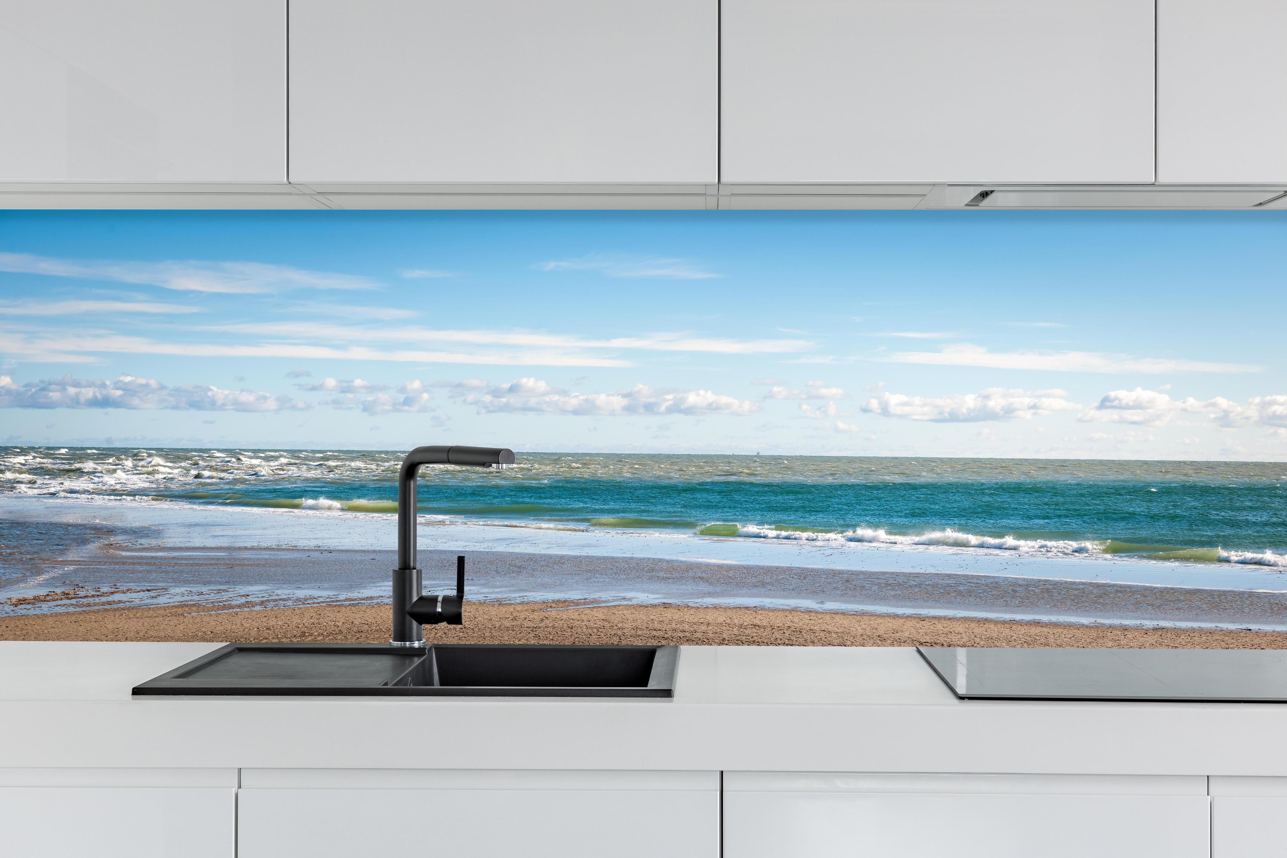 Küche - Ruhige Küstenlandschaft unter blauem Himmel mit sanften Wellen und feinem Sand hinter weißen Hochglanz-Küchenregalen und schwarzem Wasserhahn