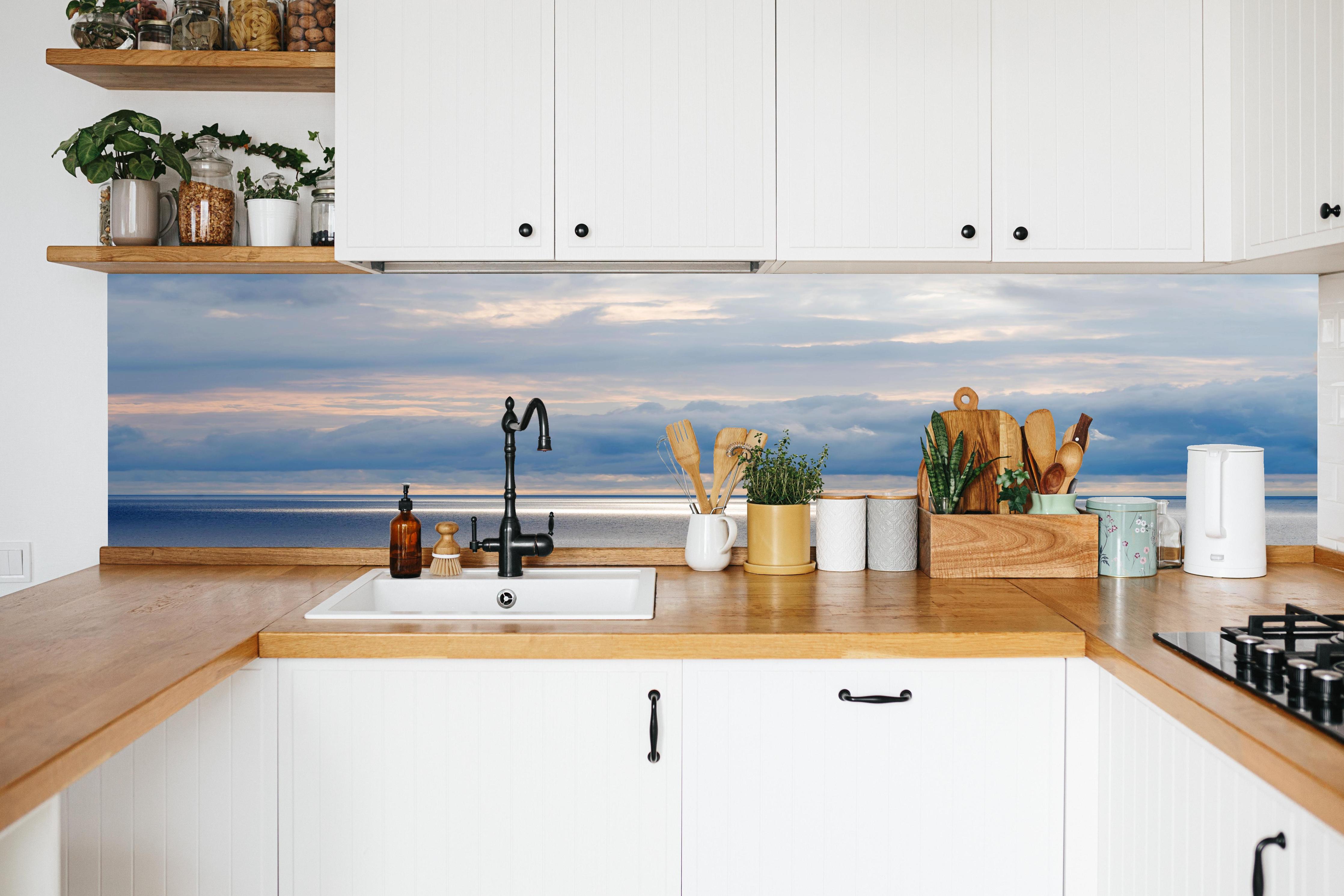 Küche - Ruhiges Blau-Grau-Meerespanorama mit sanften Wellen und Wolken hinter weißen Hochglanz-Küchenregalen und schwarzem Wasserhahn