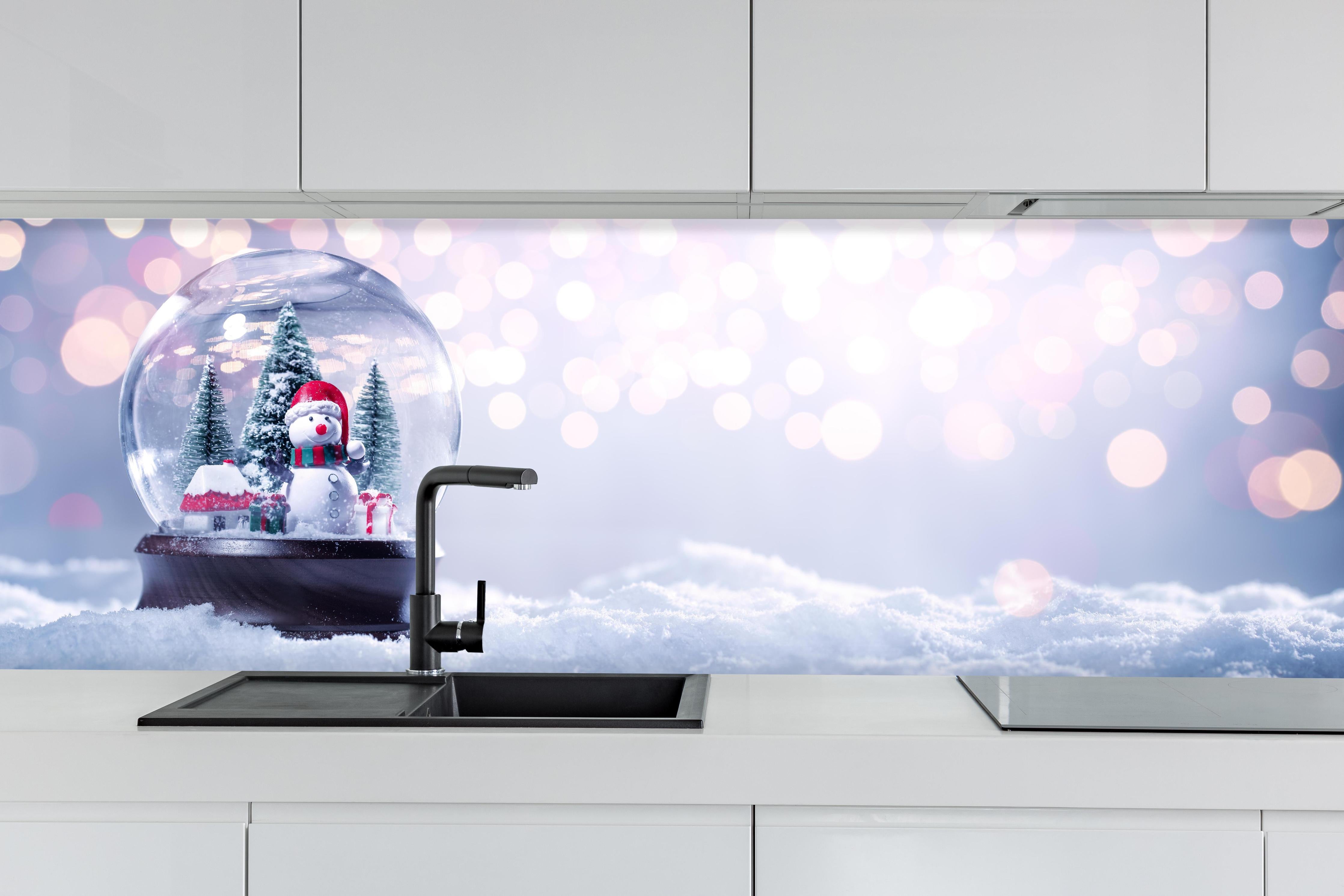 Küche - Schneekugel auf festlichem Hintergrund hinter weißen Hochglanz-Küchenregalen und schwarzem Wasserhahn