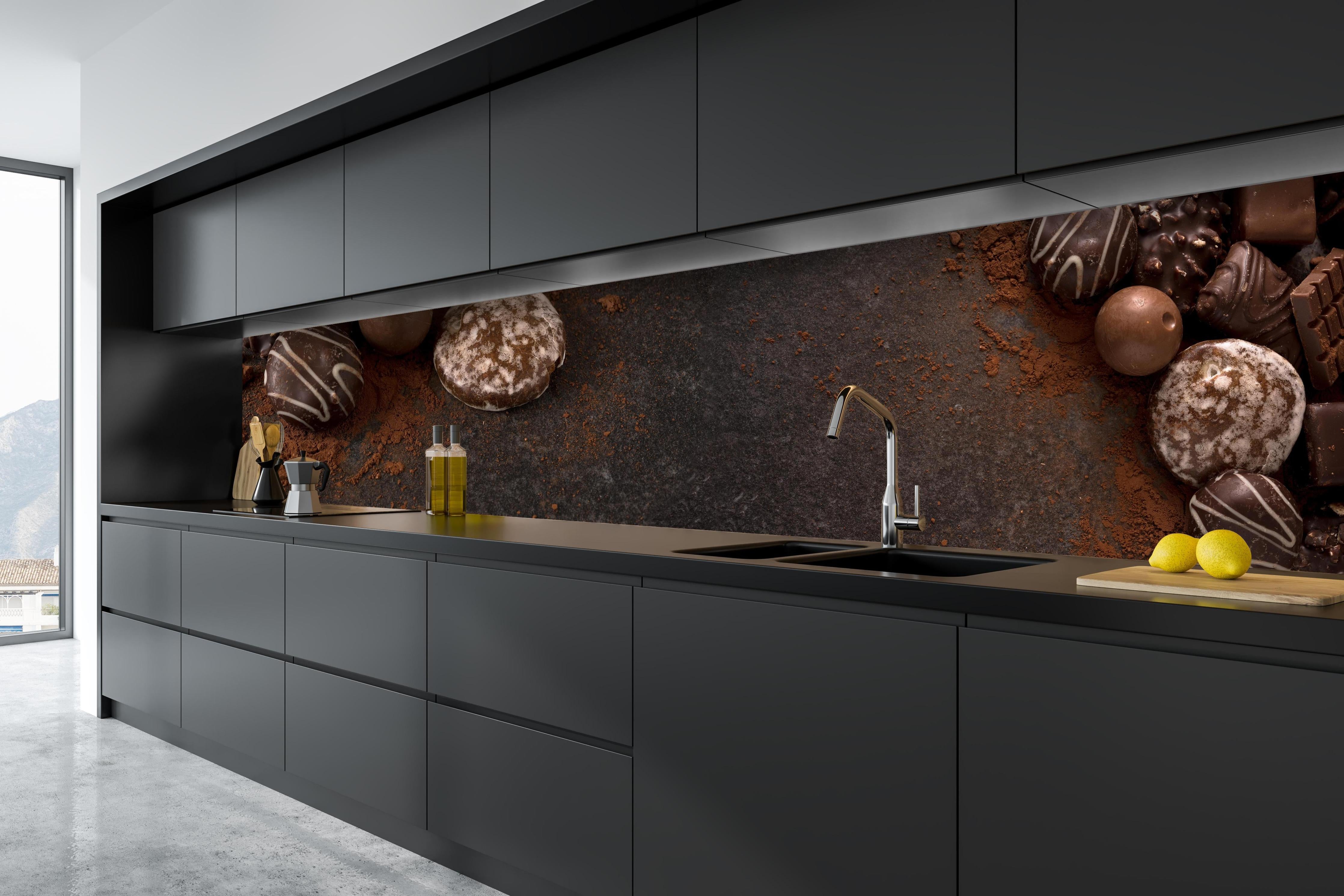 Küche - Schokoladenpralinen auf Schieferuntergrund hinter weißen Hochglanz-Küchenregalen und schwarzem Wasserhahn