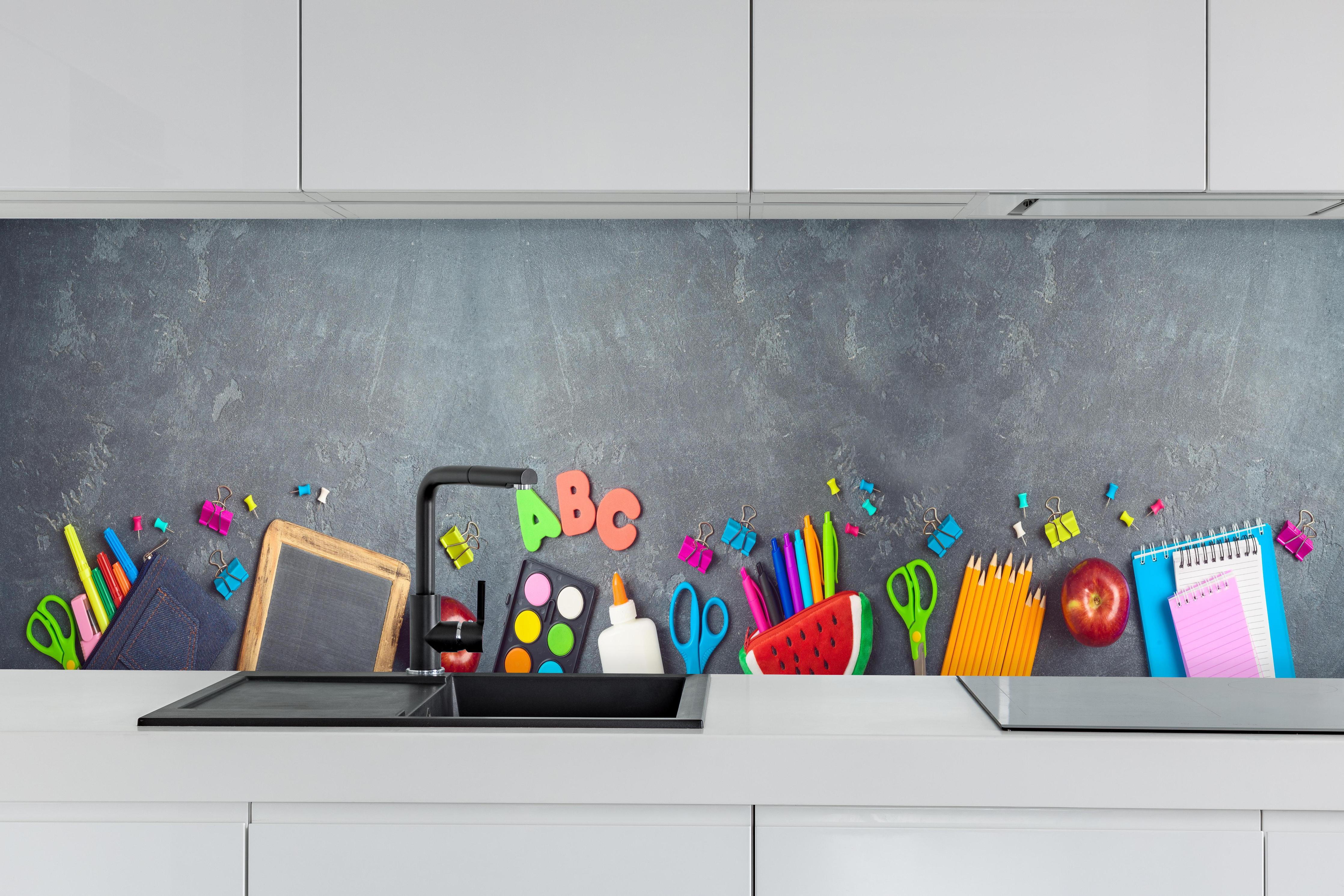 Küche - Schulbedarf auf Tafel für den Schulstart hinter weißen Hochglanz-Küchenregalen und schwarzem Wasserhahn