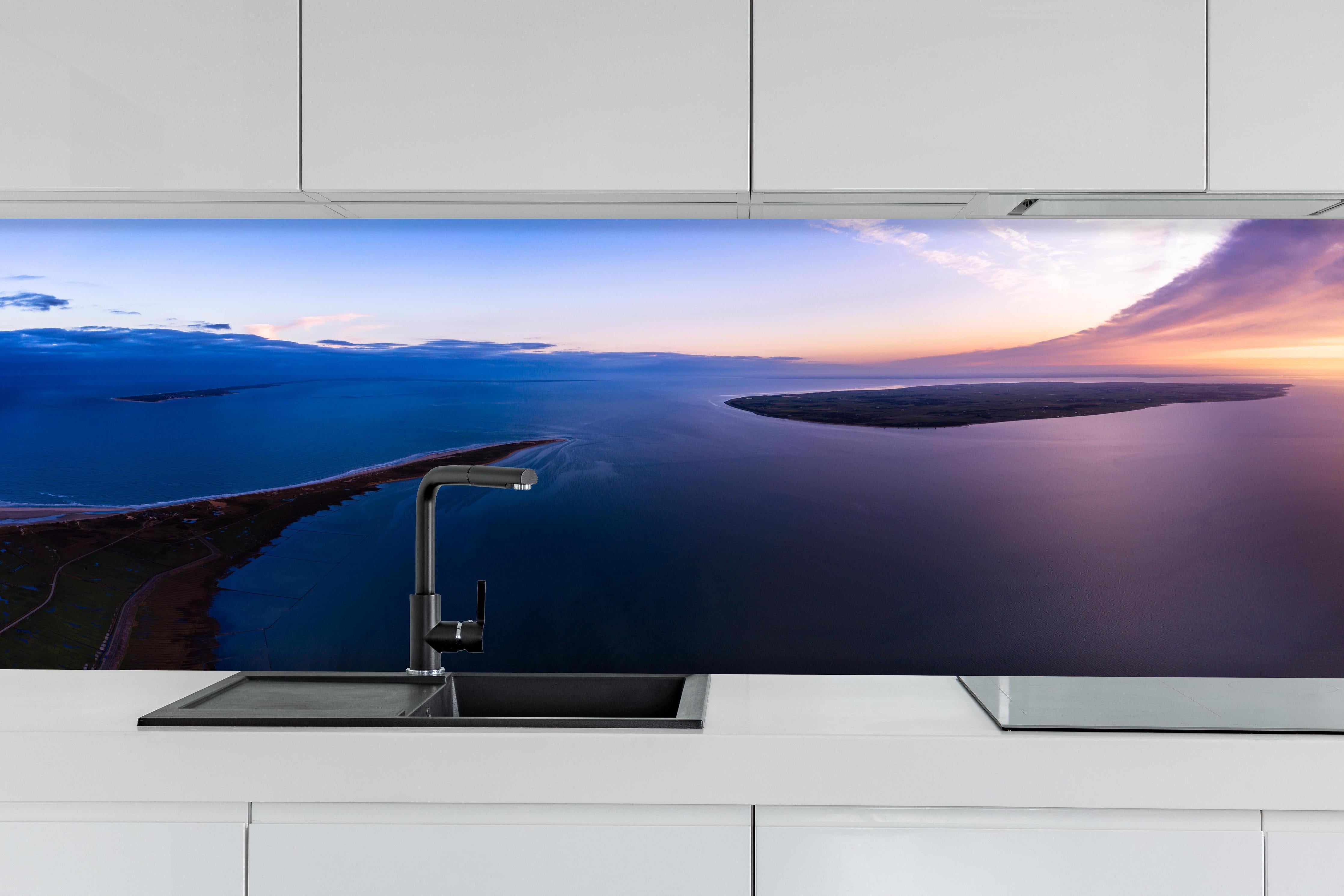 Küche - Spektakulärer Sonnenuntergang über ruhigem Gewässer und unberührten Inseln hinter weißen Hochglanz-Küchenregalen und schwarzem Wasserhahn