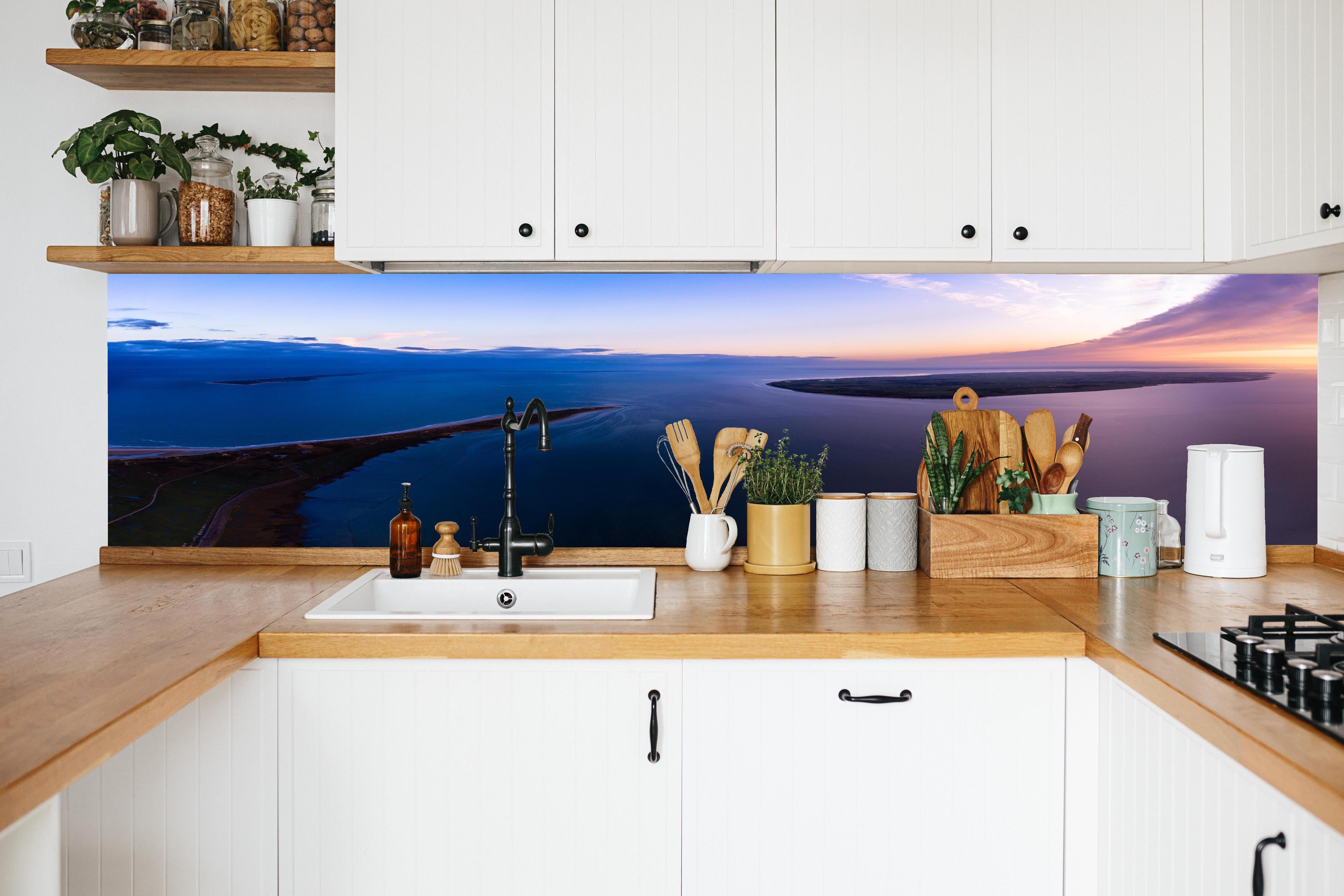 Küche - Spektakulärer Sonnenuntergang über ruhigem Gewässer und unberührten Inseln hinter weißen Hochglanz-Küchenregalen und schwarzem Wasserhahn