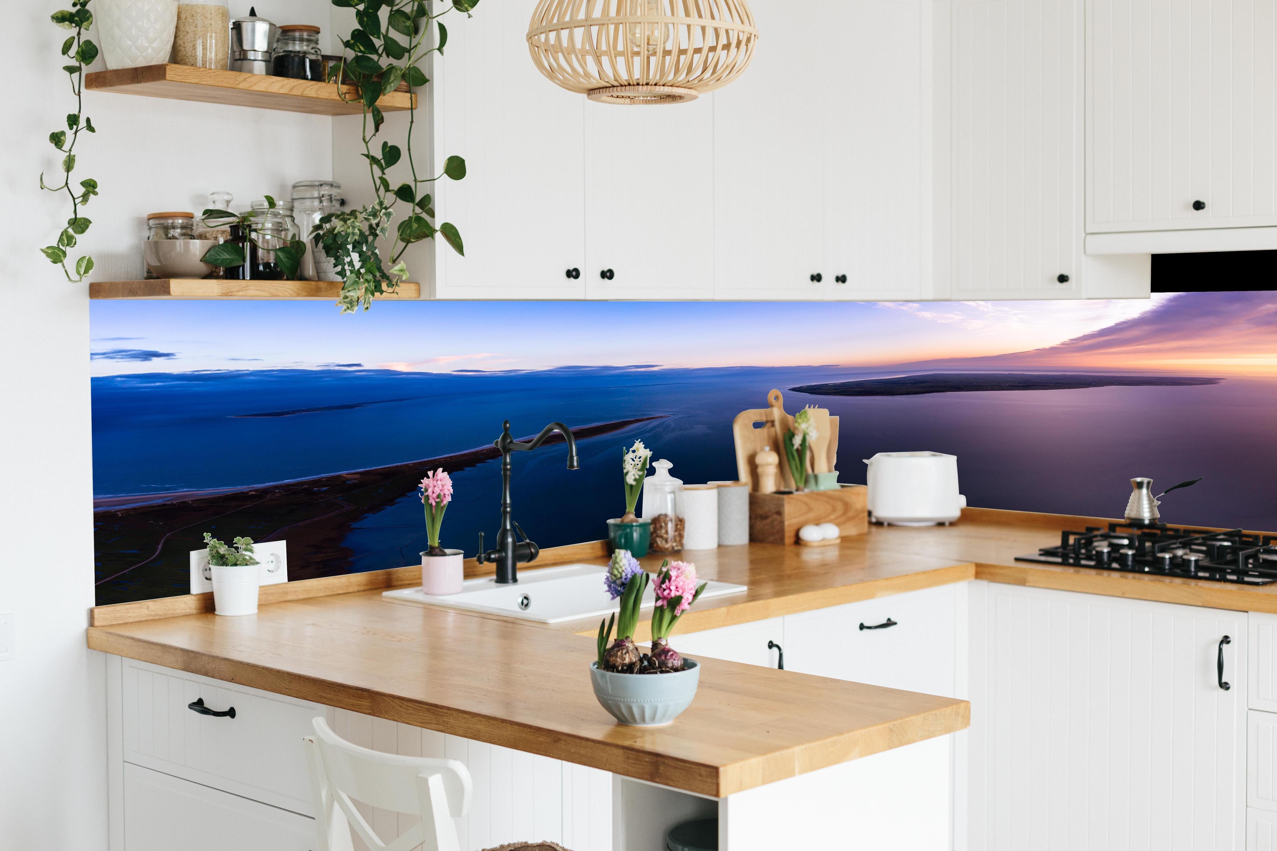 Küche - Spektakulärer Sonnenuntergang über ruhigem Gewässer und unberührten Inseln hinter weißen Hochglanz-Küchenregalen und schwarzem Wasserhahn