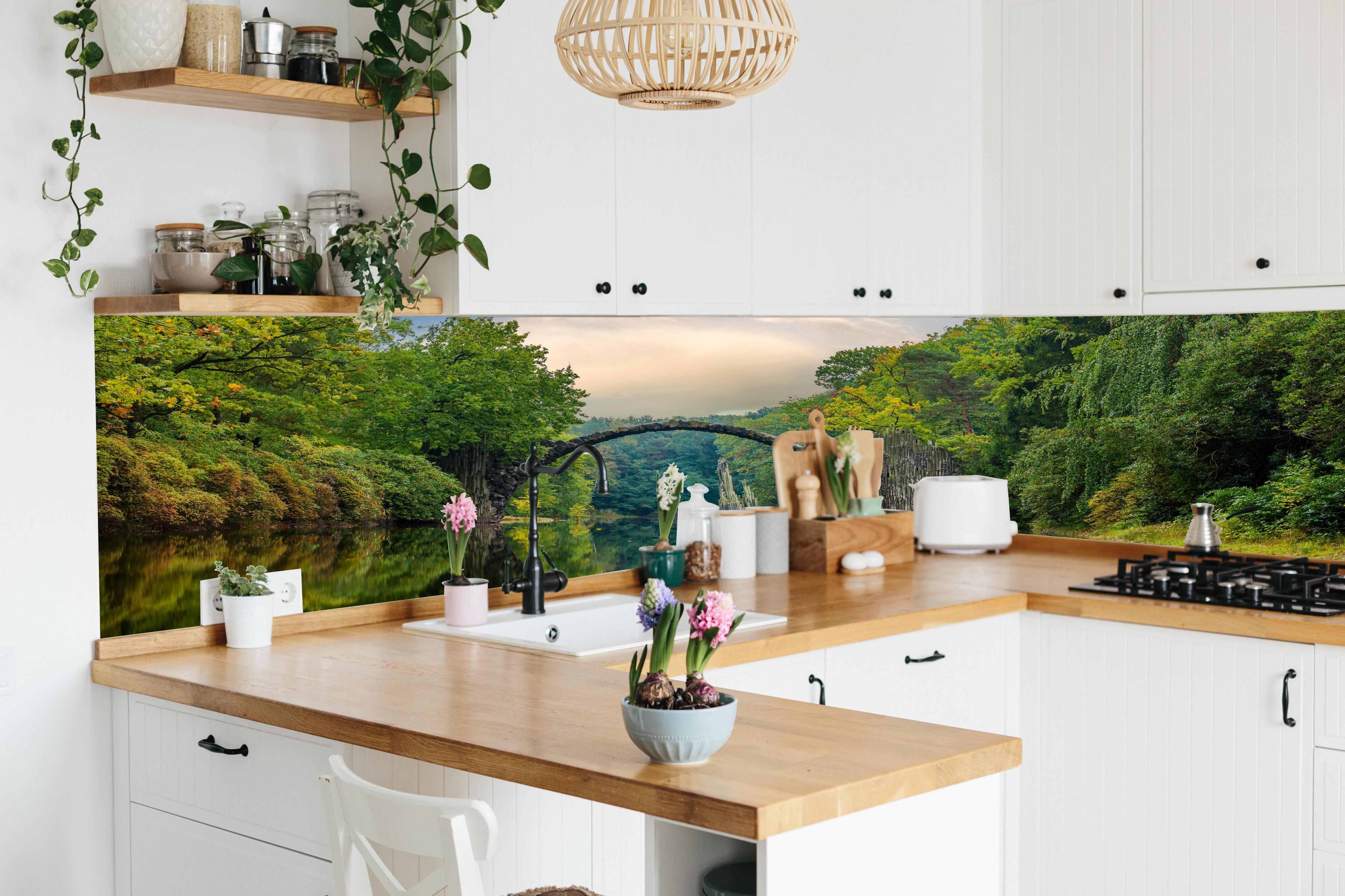 Küche - Steinbrücke über Fluss im Wald hinter weißen Hochglanz-Küchenregalen und schwarzem Wasserhahn