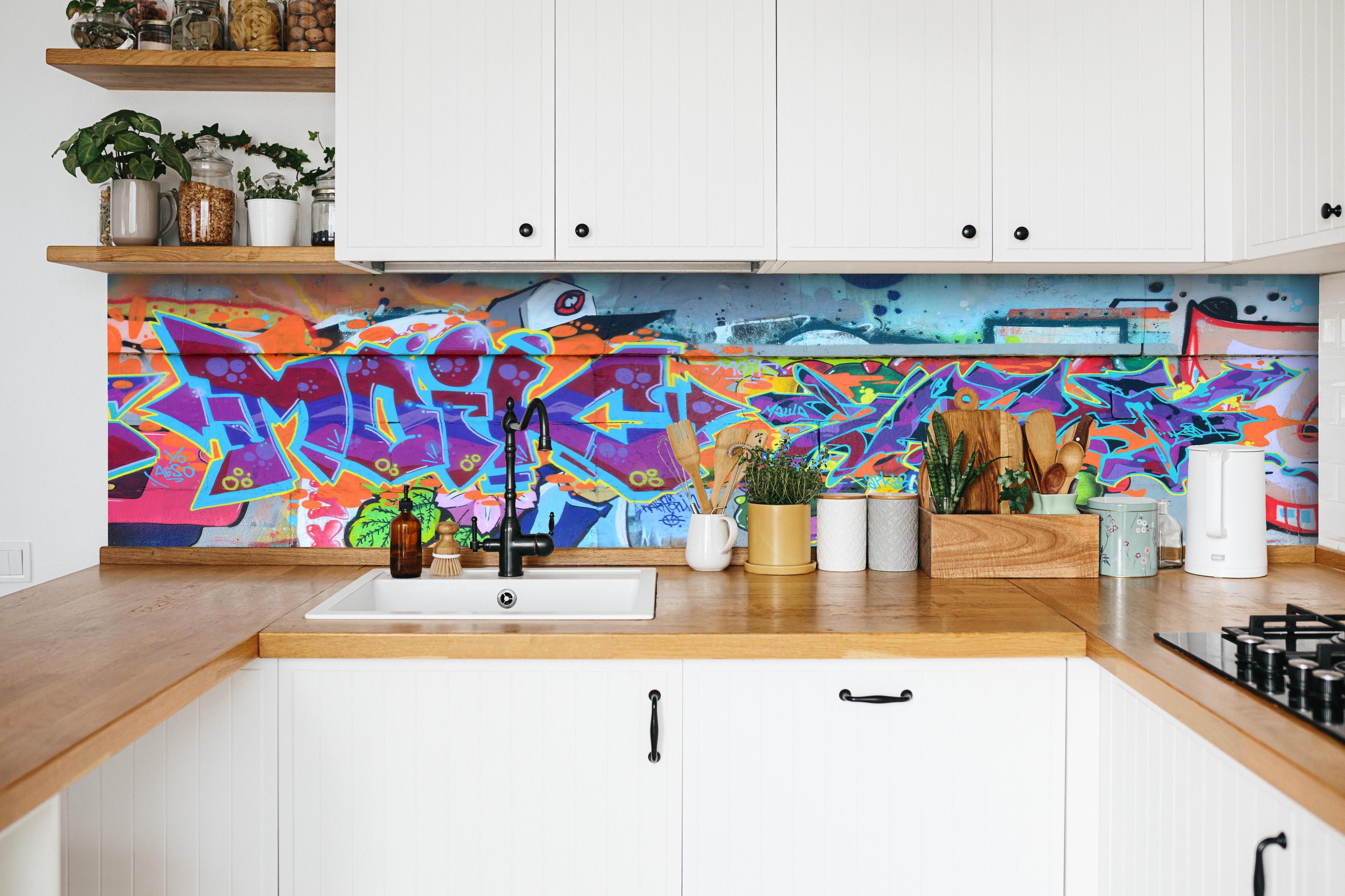 Küche - Street Art Graffiti in Lila-Tönen hinter weißen Hochglanz-Küchenregalen und schwarzem Wasserhahn