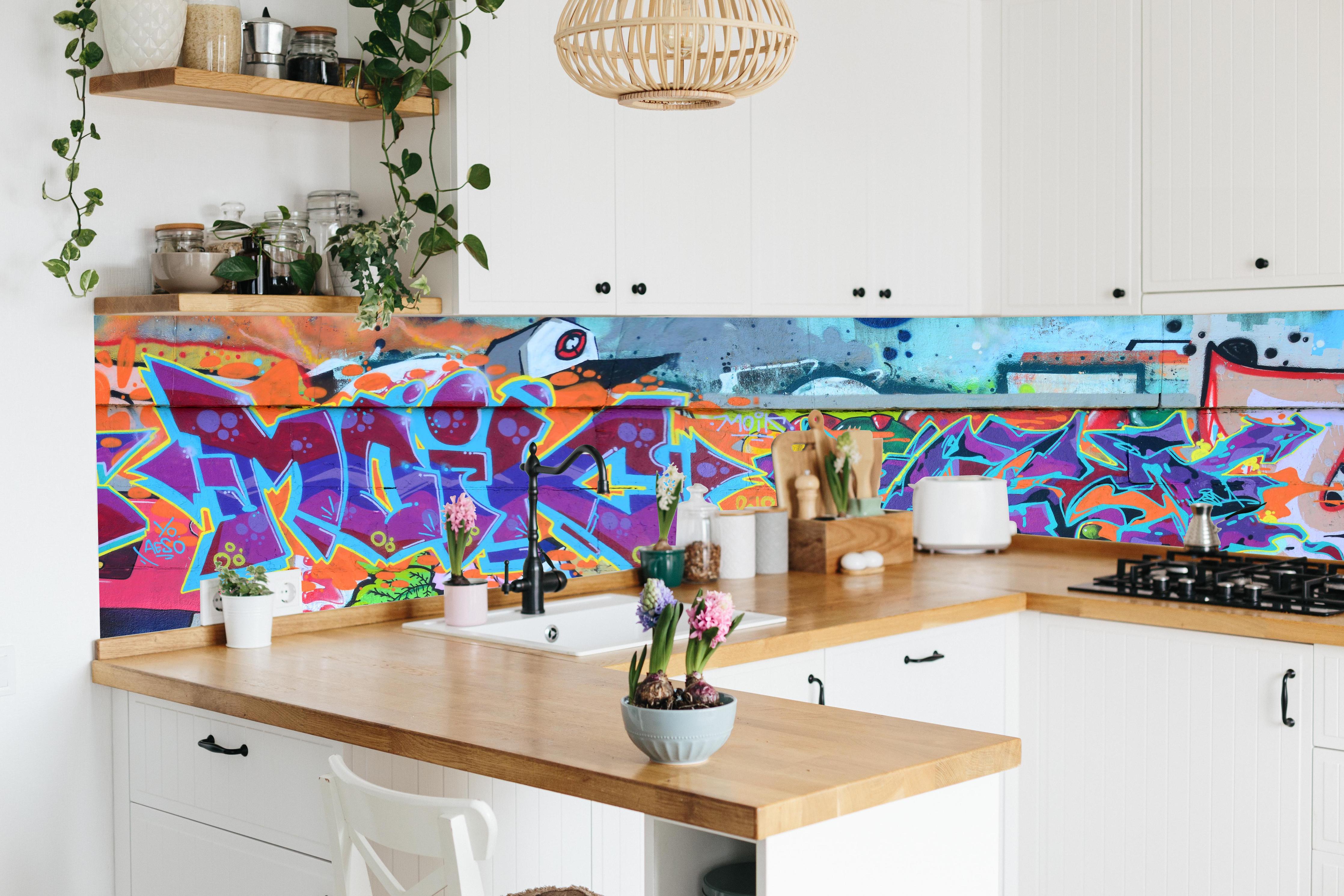Küche - Street Art Graffiti in Lila-Tönen hinter weißen Hochglanz-Küchenregalen und schwarzem Wasserhahn
