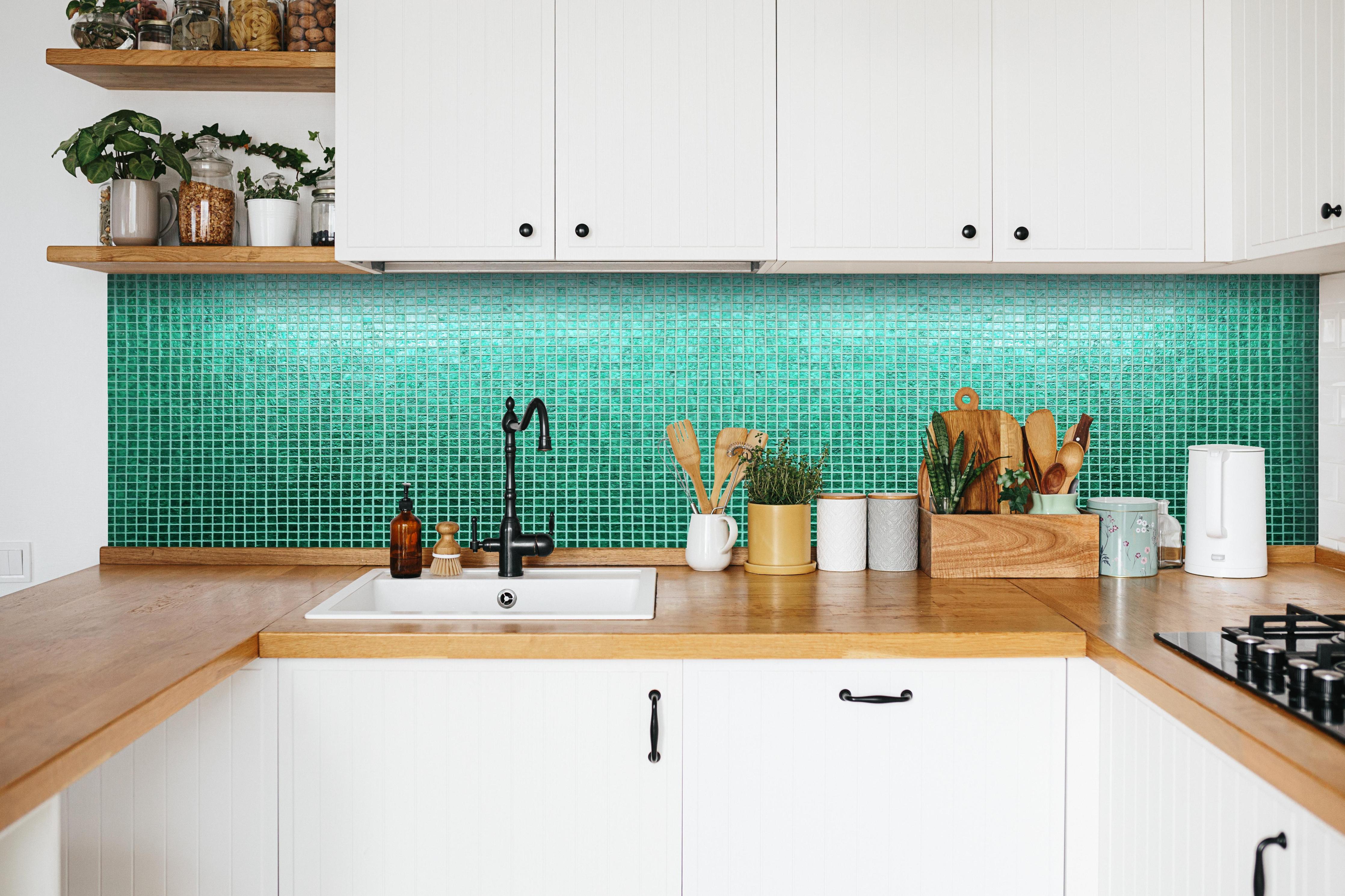 Küche - Strukturierte grüne Fliesenmosaik Textur hinter weißen Hochglanz-Küchenregalen und schwarzem Wasserhahn