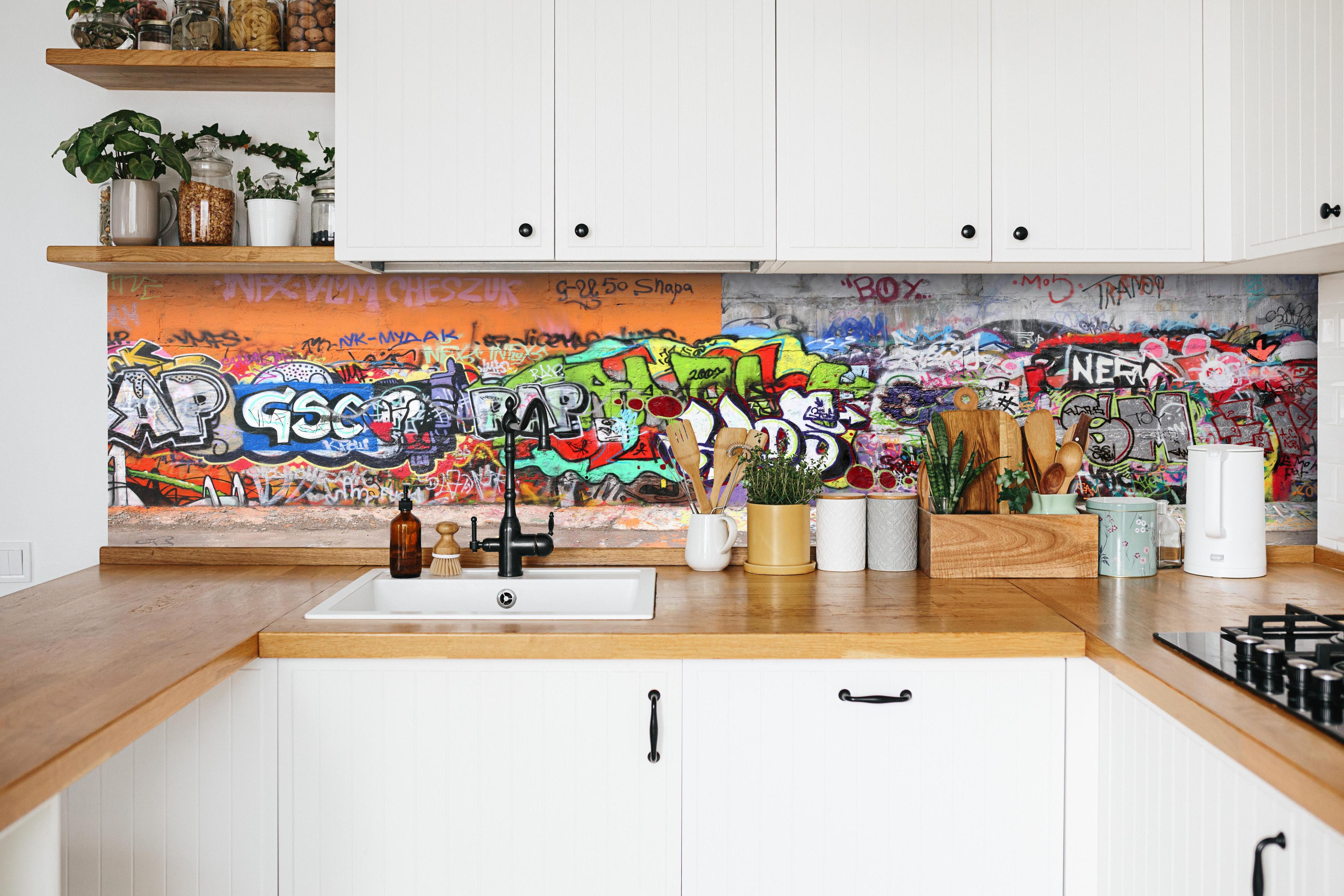 Küche - Textur Urbaner Graffiti-Art Streetstyle hinter weißen Hochglanz-Küchenregalen und schwarzem Wasserhahn