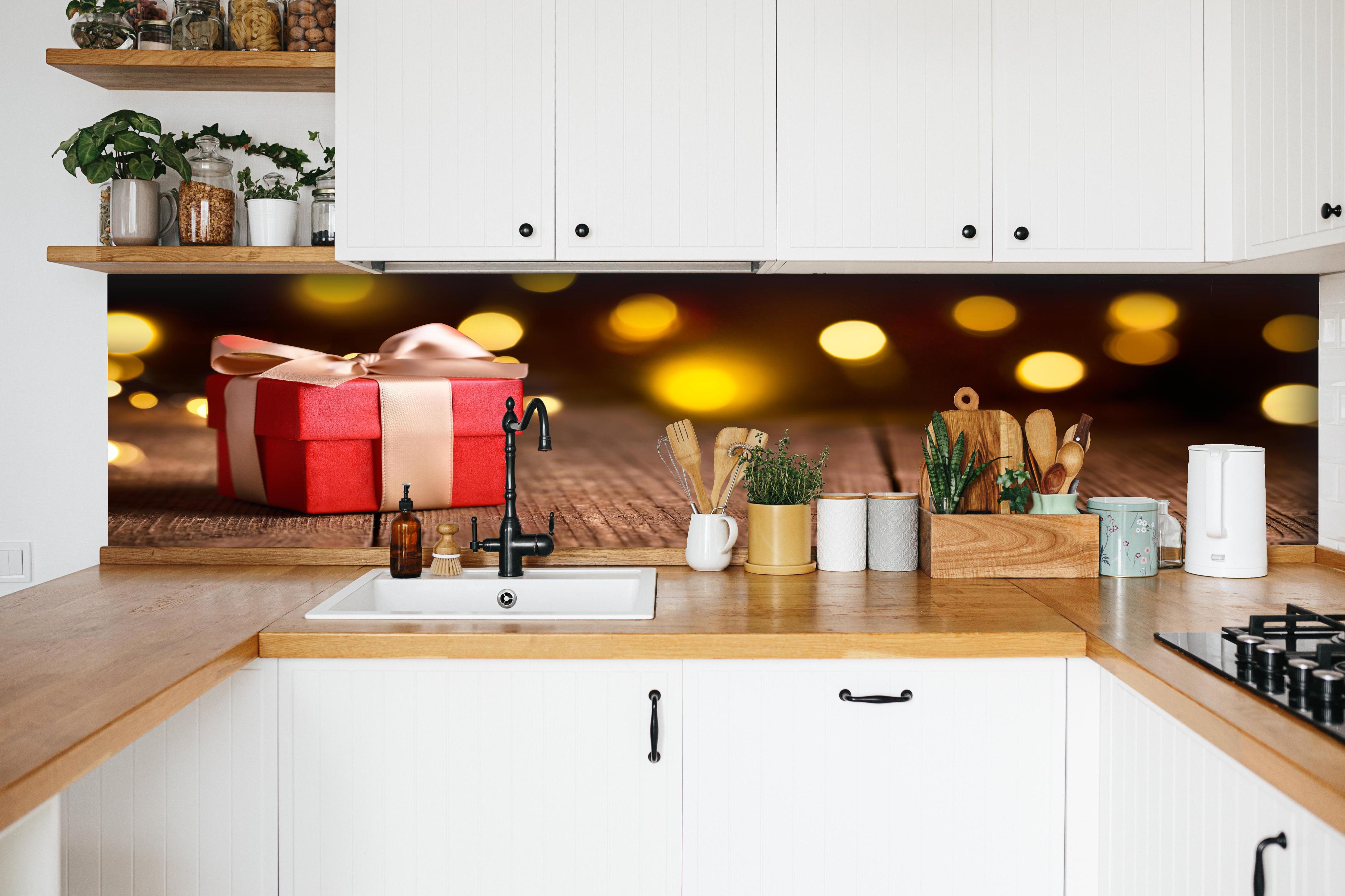 Küche - Weihnachtsgeschenk auf festlichem Hintergrund hinter weißen Hochglanz-Küchenregalen und schwarzem Wasserhahn
