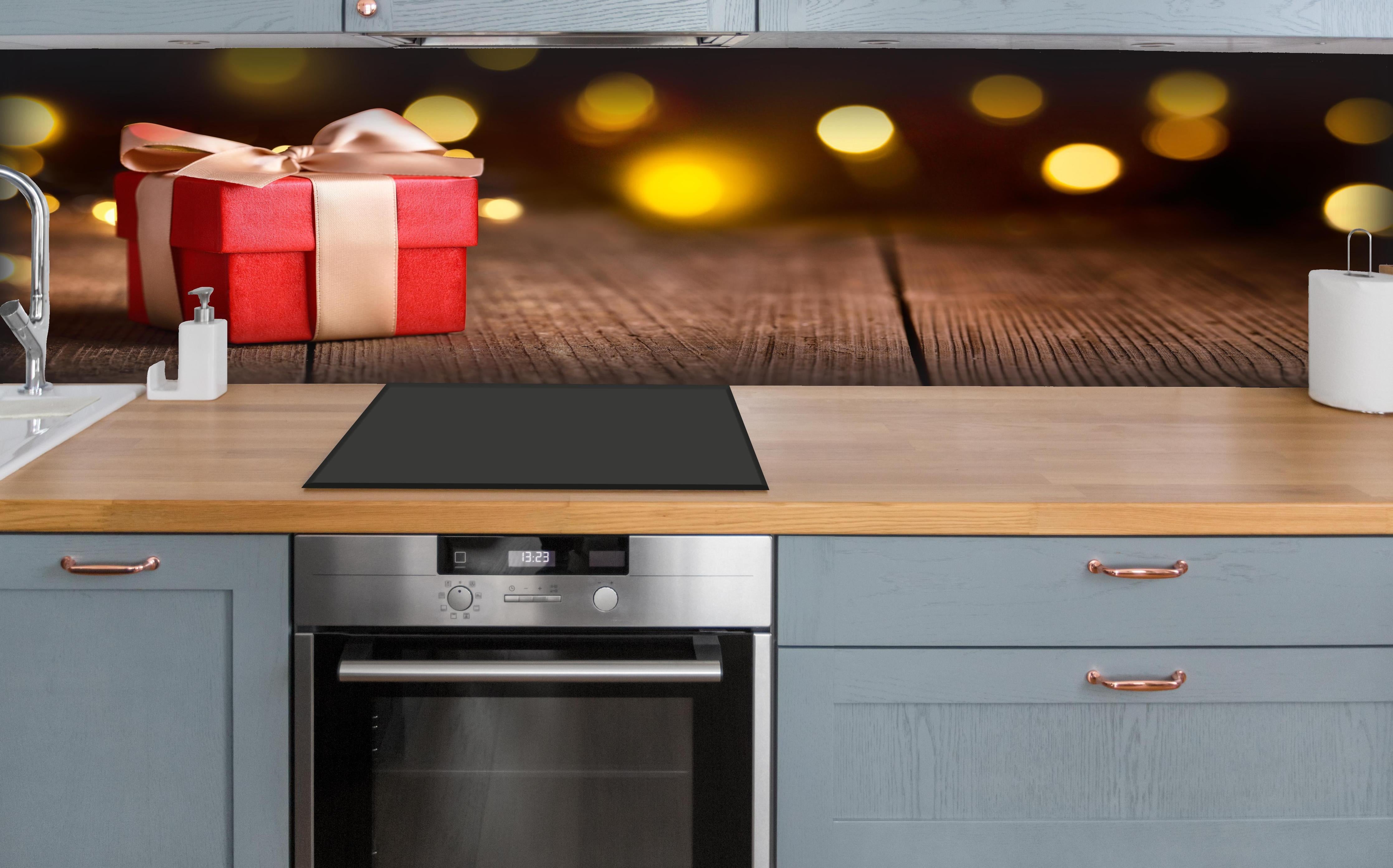 Küche - Weihnachtsgeschenk auf festlichem Hintergrund hinter weißen Hochglanz-Küchenregalen und schwarzem Wasserhahn