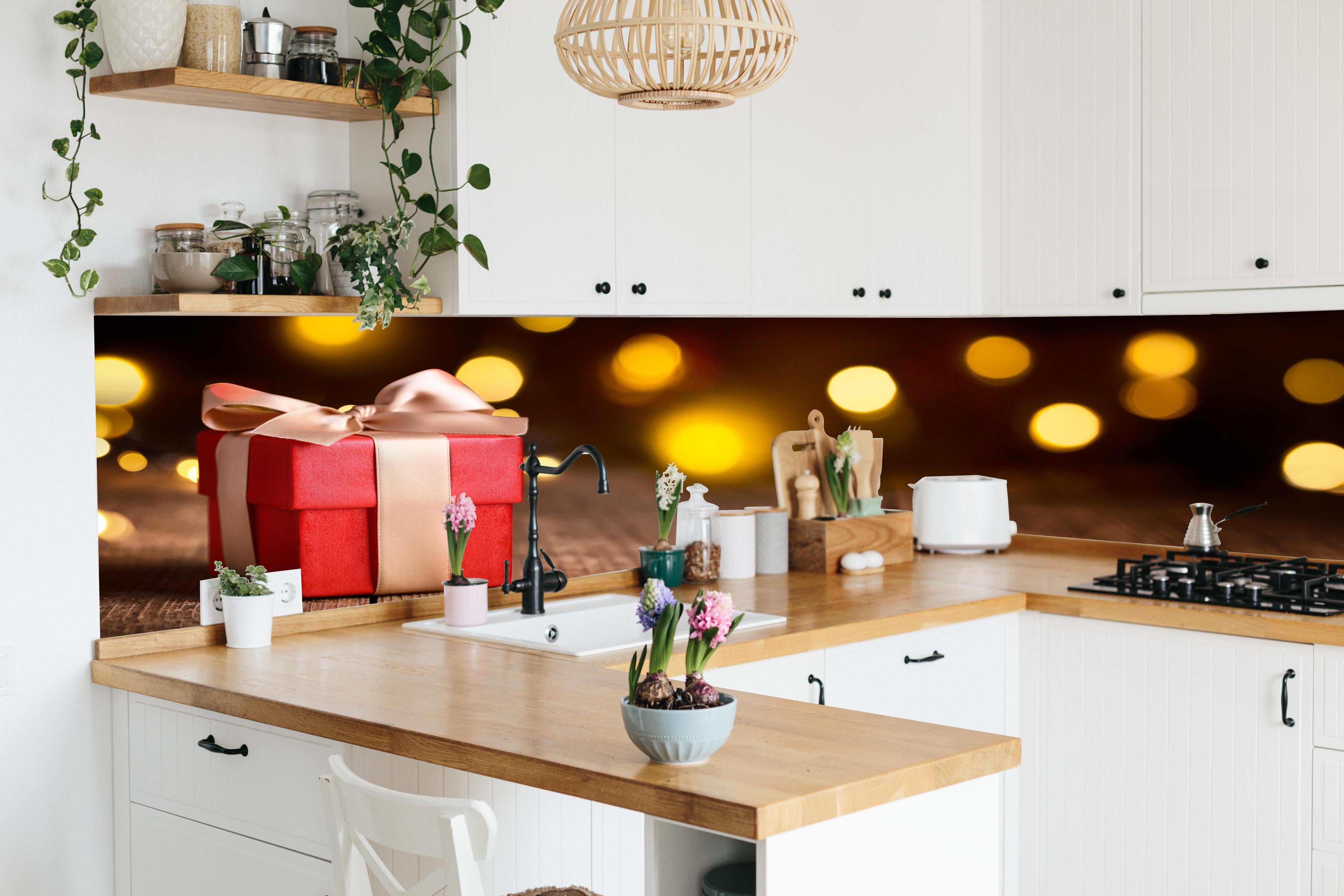 Küche - Weihnachtsgeschenk auf festlichem Hintergrund hinter weißen Hochglanz-Küchenregalen und schwarzem Wasserhahn