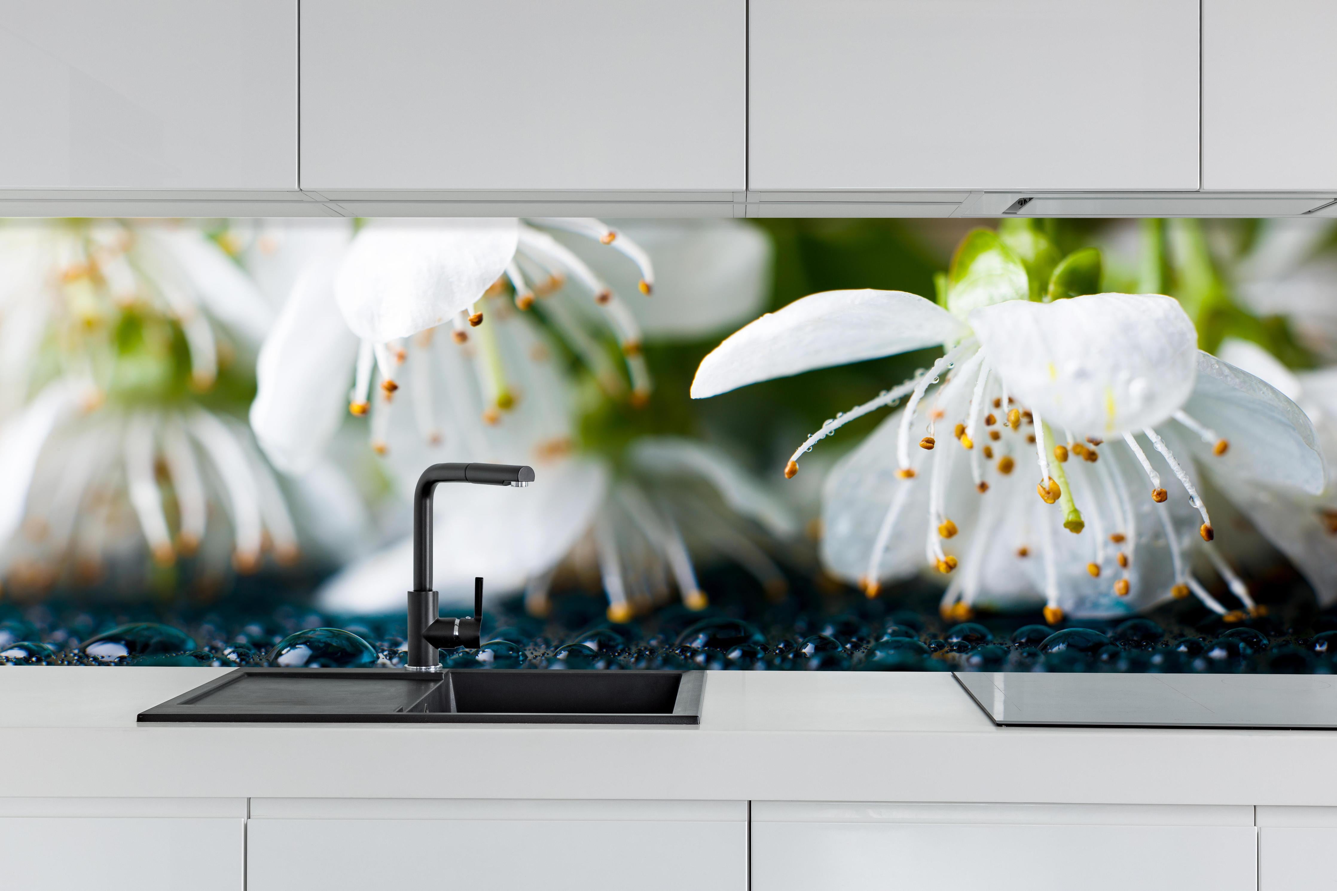 Küche - Weiße blühende Frühlingsblumen hinter weißen Hochglanz-Küchenregalen und schwarzem Wasserhahn