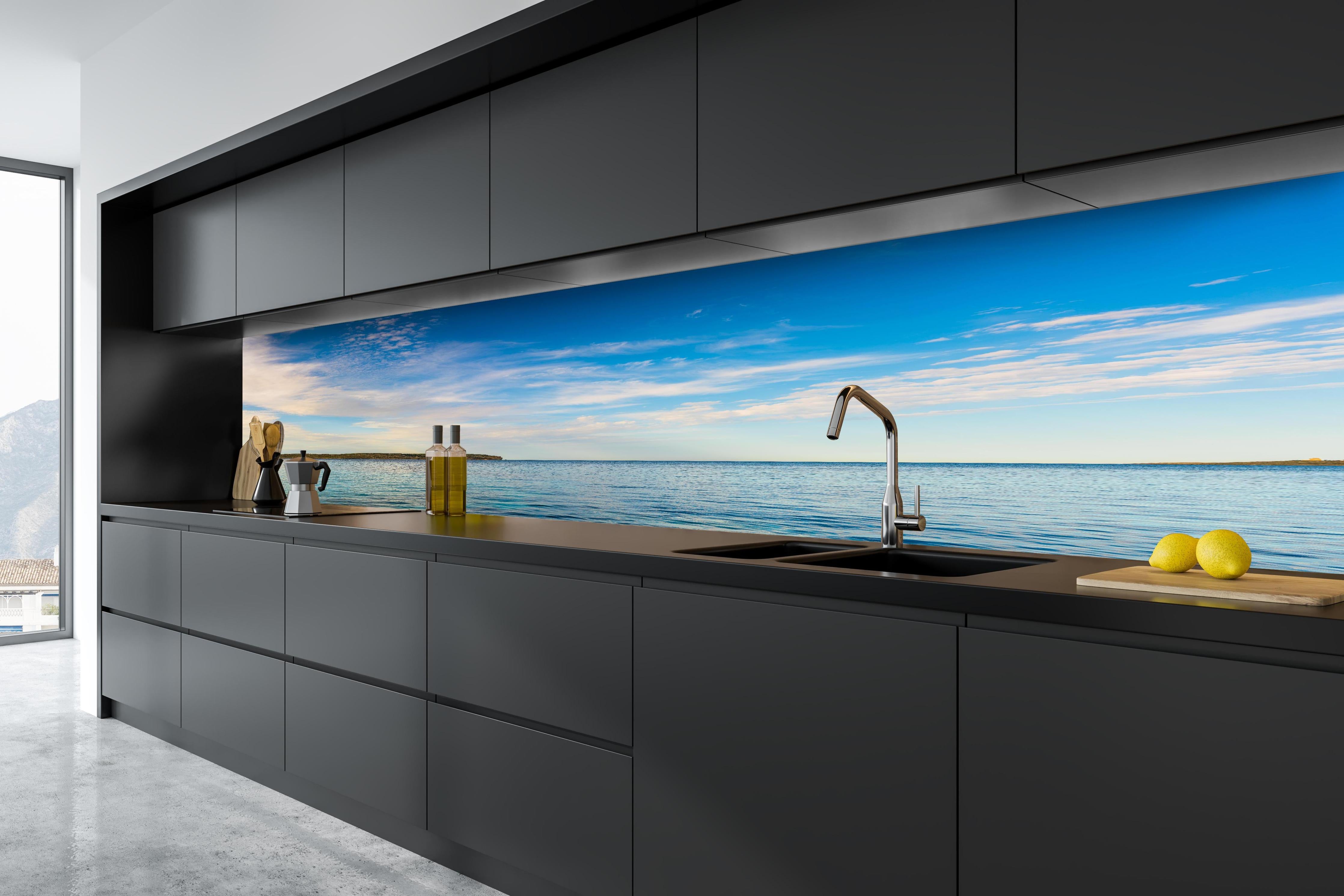 Küche - Weite und ruhige Meerelandschaft unter einem strahlend blauen Himmel hinter weißen Hochglanz-Küchenregalen und schwarzem Wasserhahn