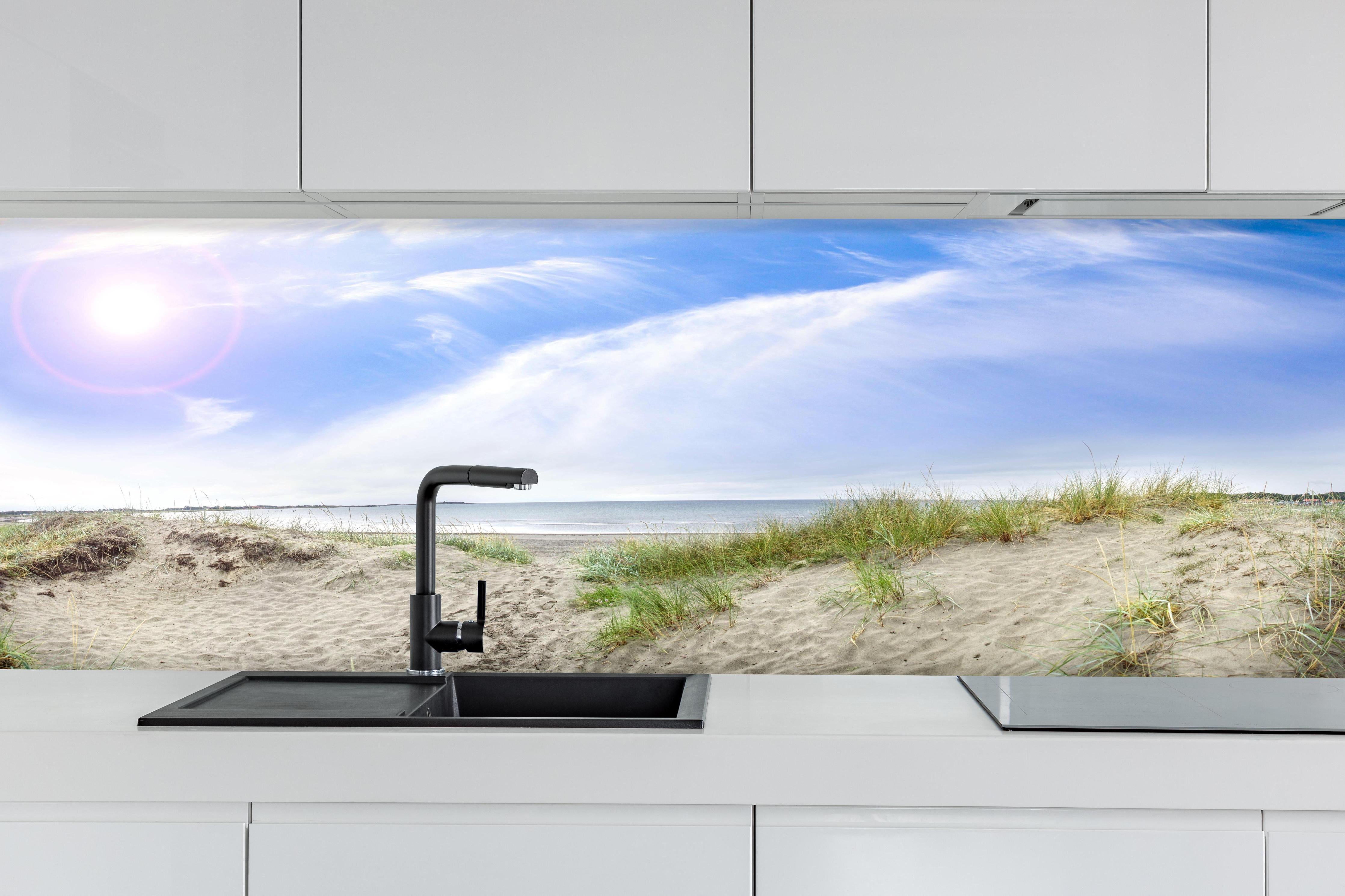 Küche - Weitläufige Strandlandschaft mit sanften Dünen, Himmel und ruhigem Wasser hinter weißen Hochglanz-Küchenregalen und schwarzem Wasserhahn