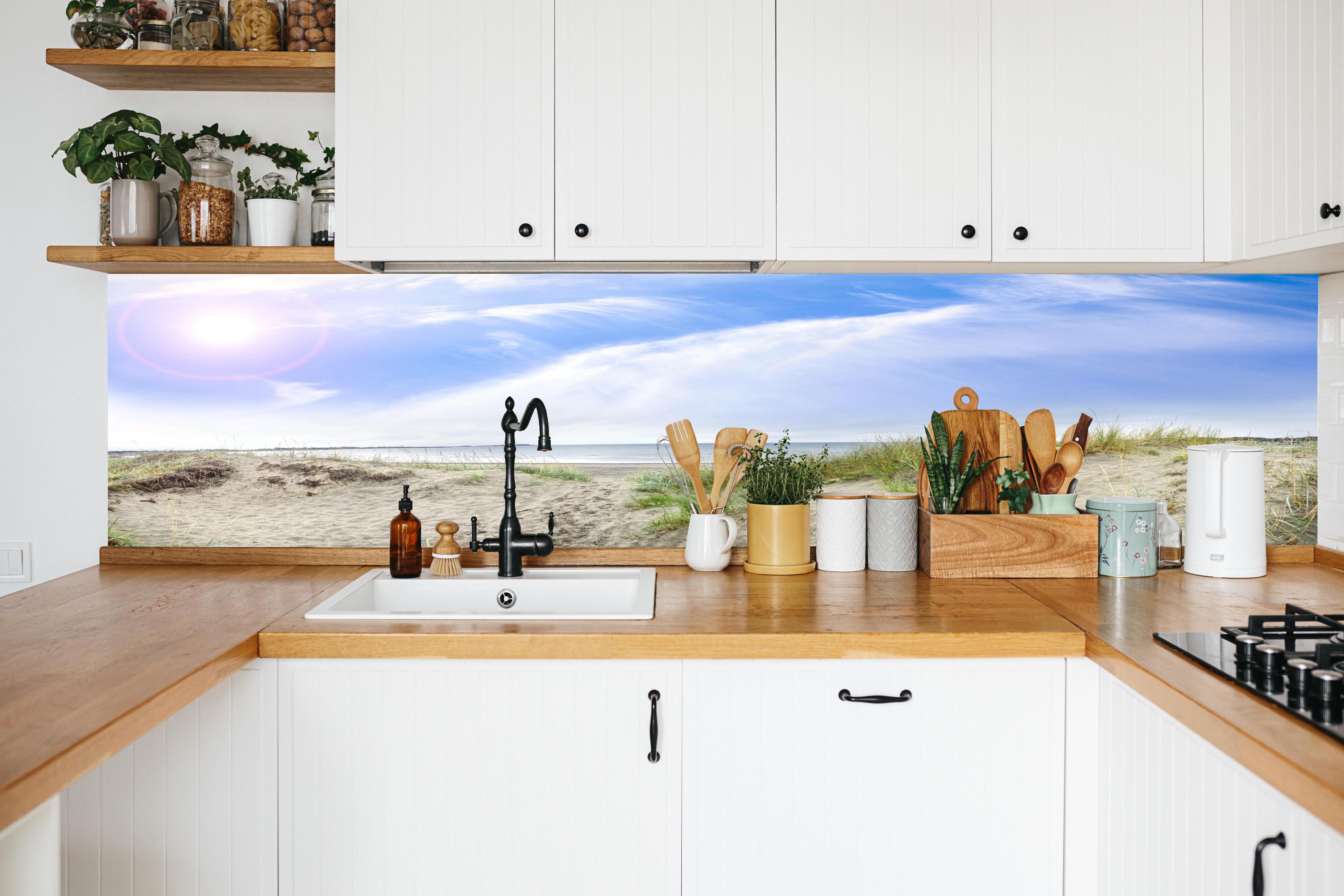 Küche - Weitläufige Strandlandschaft mit sanften Dünen, Himmel und ruhigem Wasser hinter weißen Hochglanz-Küchenregalen und schwarzem Wasserhahn