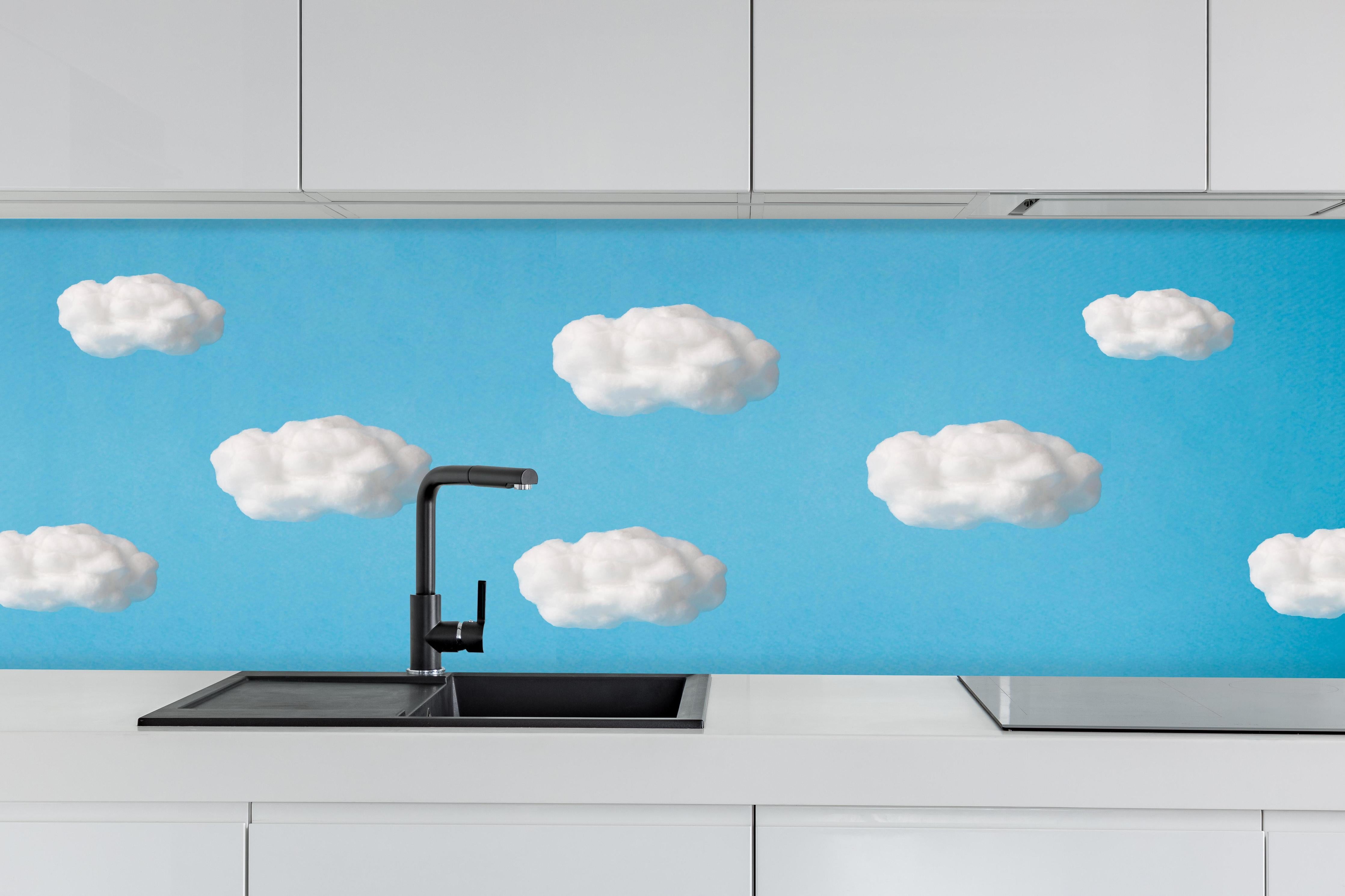 Küche - Wolke aus Watte auf himmelblauem Hintergrund hinter weißen Hochglanz-Küchenregalen und schwarzem Wasserhahn