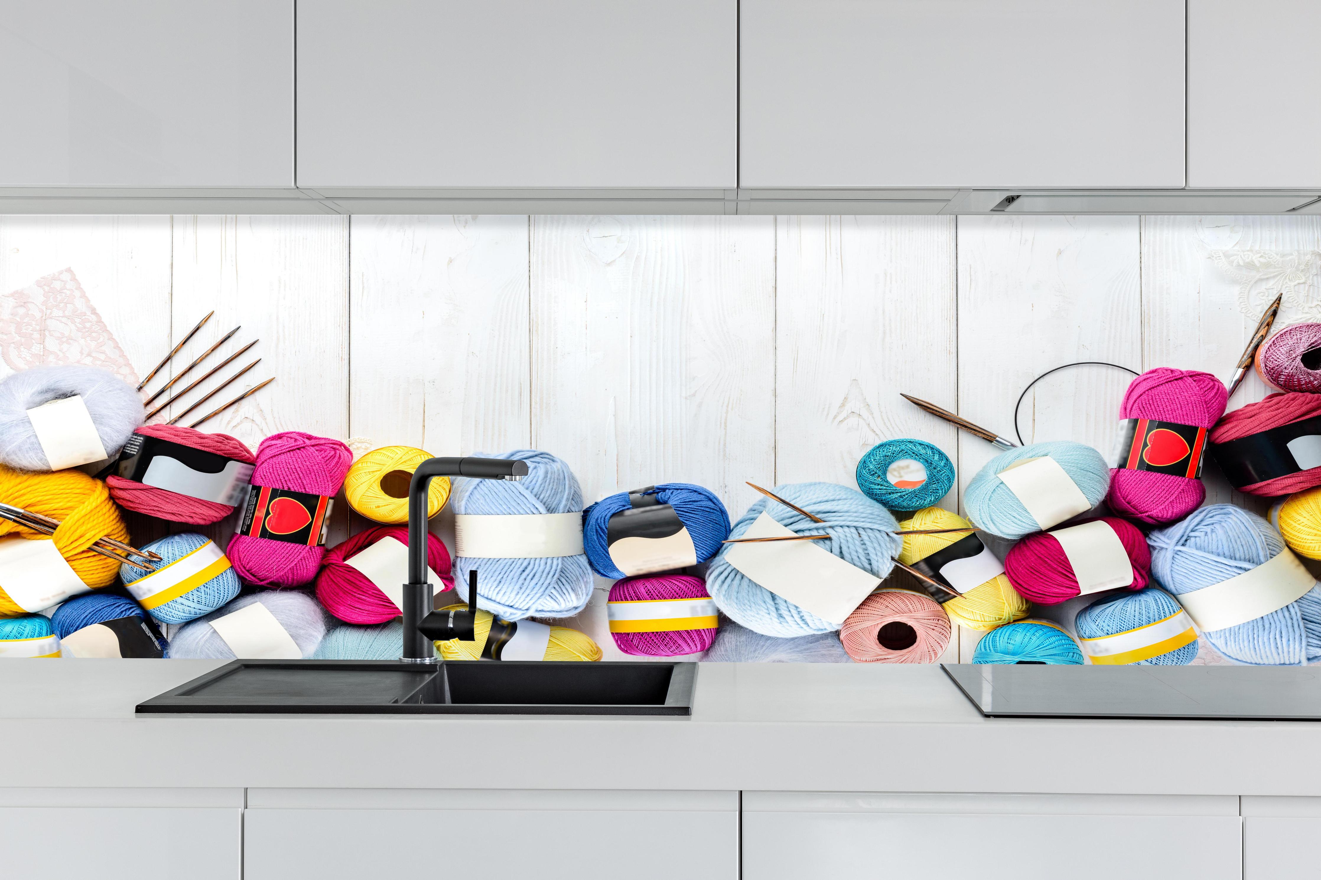 Küche - Wolle und Stricknadeln auf Holzhintergrund hinter weißen Hochglanz-Küchenregalen und schwarzem Wasserhahn