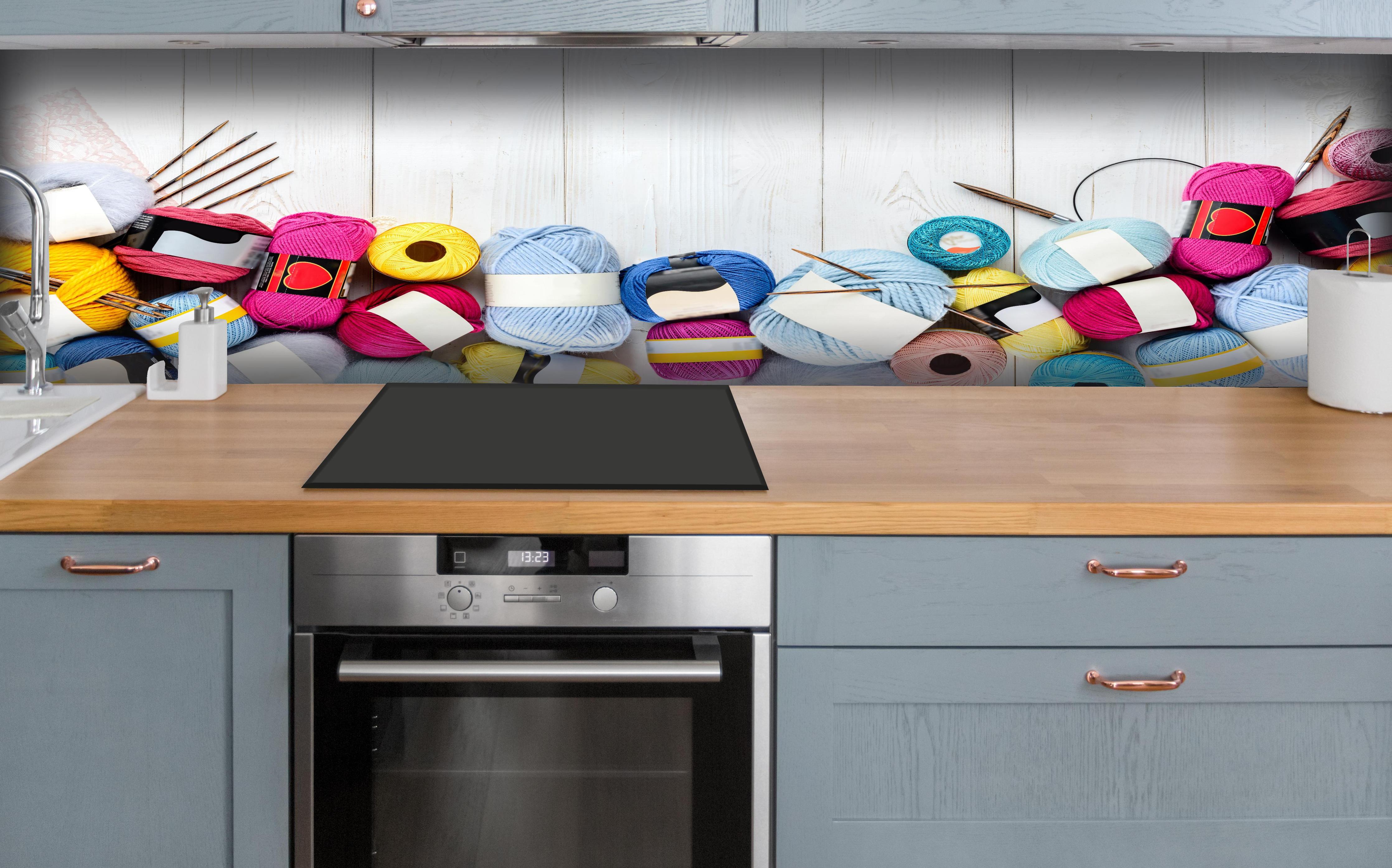 Küche - Wolle und Stricknadeln auf Holzhintergrund hinter weißen Hochglanz-Küchenregalen und schwarzem Wasserhahn