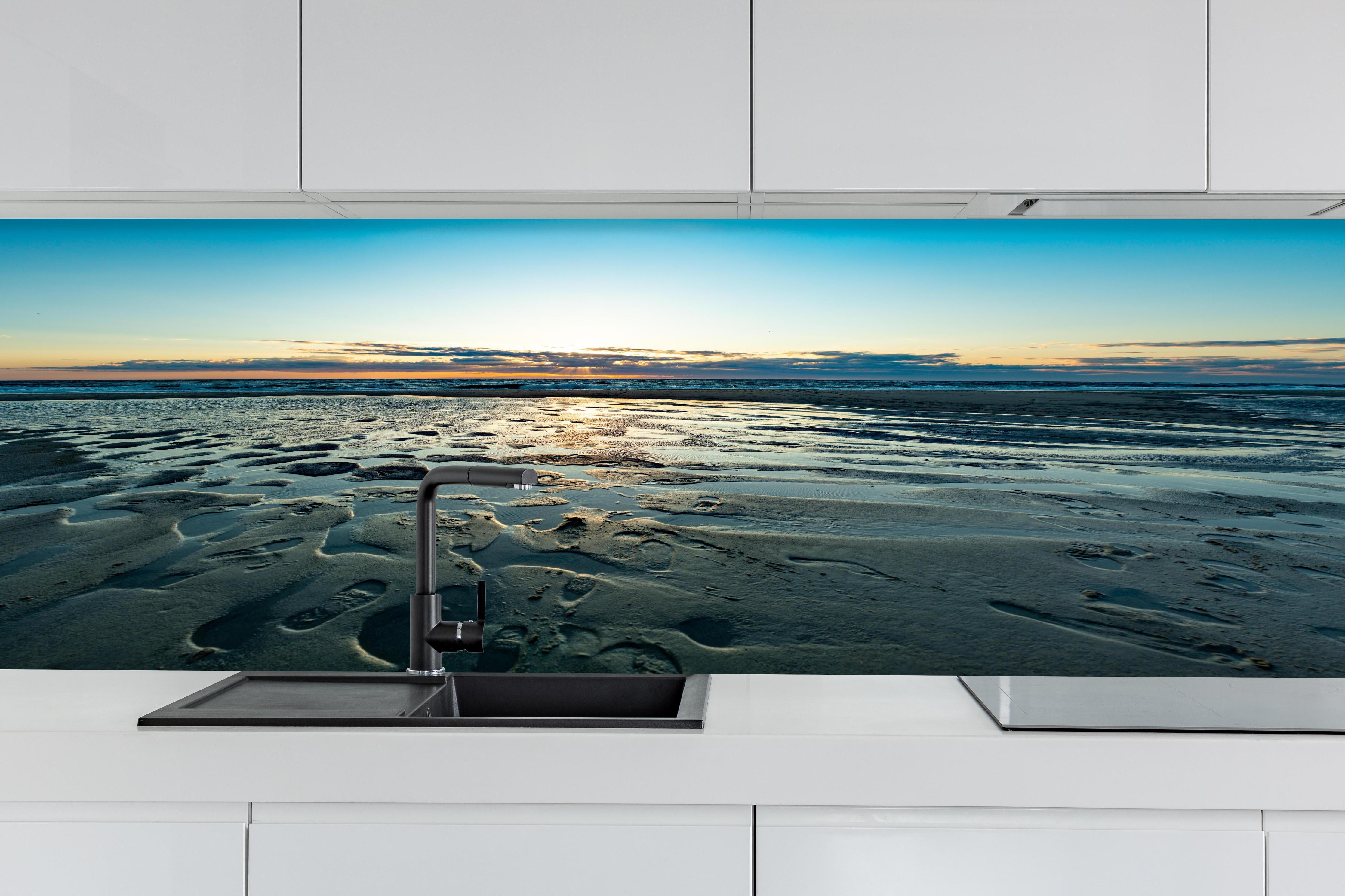 Küche - Wunderschöne blaue und orange Strandlandschaft mit Sonnenuntergang hinter weißen Hochglanz-Küchenregalen und schwarzem Wasserhahn