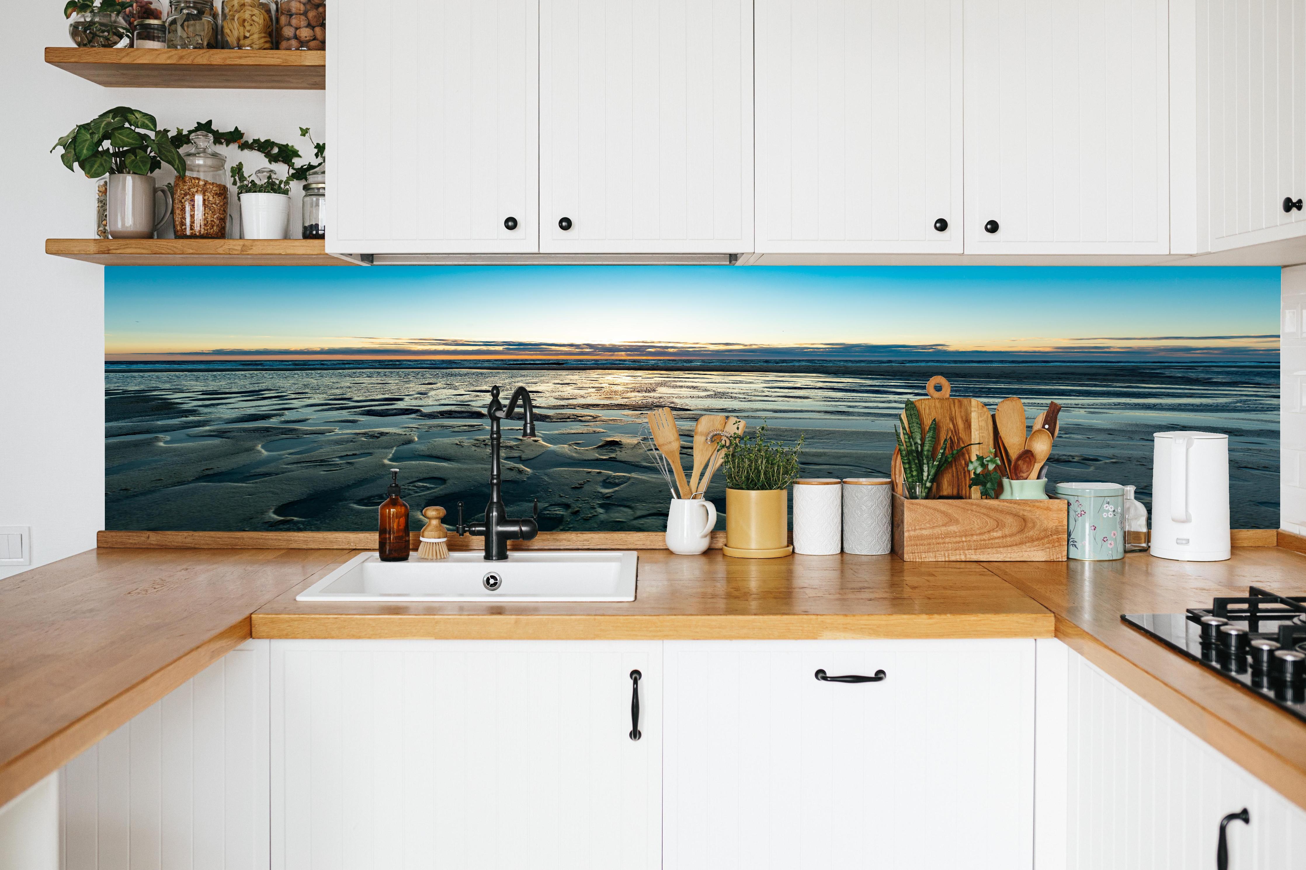 Küche - Wunderschöne blaue und orange Strandlandschaft mit Sonnenuntergang hinter weißen Hochglanz-Küchenregalen und schwarzem Wasserhahn