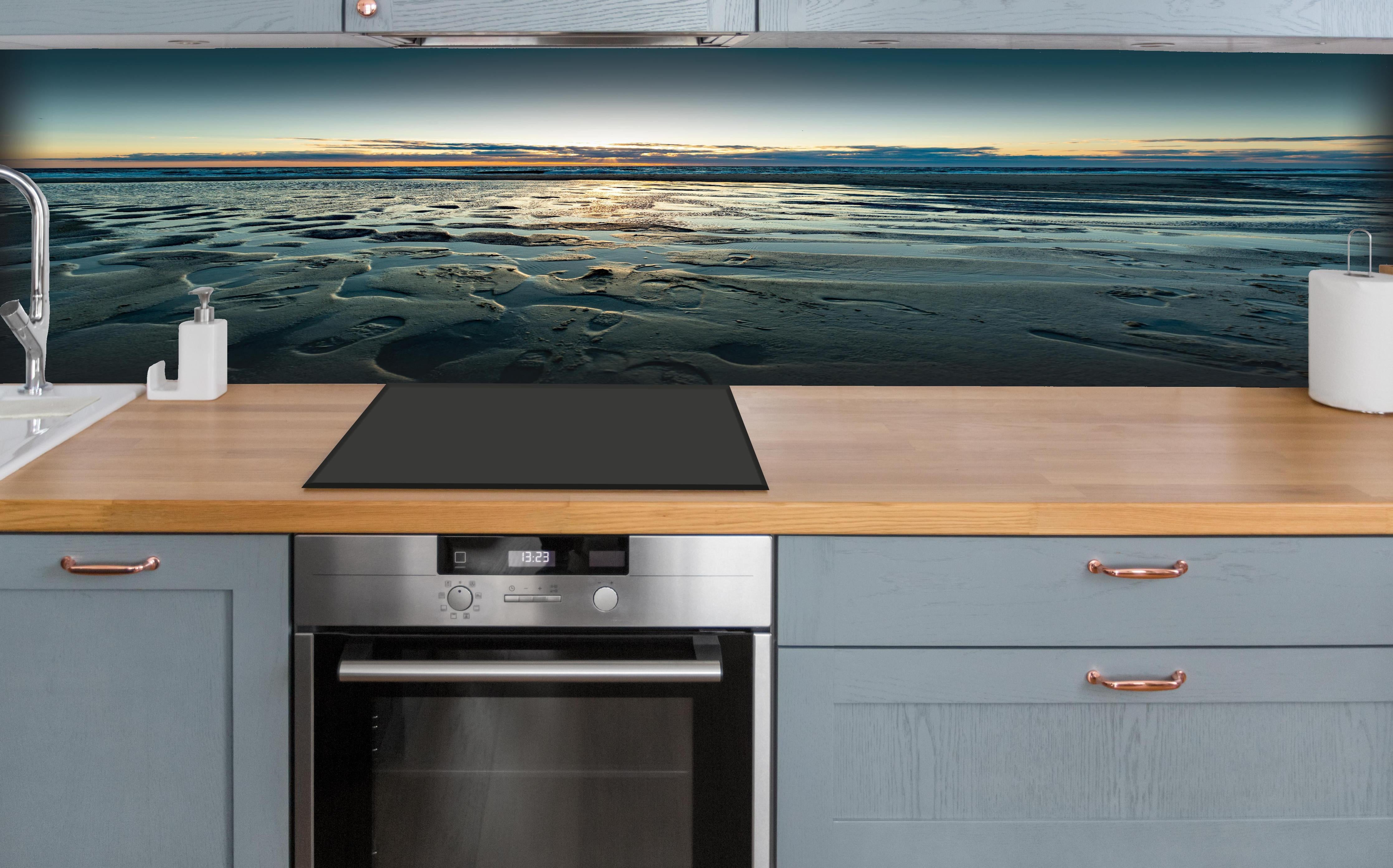 Küche - Wunderschöne blaue und orange Strandlandschaft mit Sonnenuntergang hinter weißen Hochglanz-Küchenregalen und schwarzem Wasserhahn