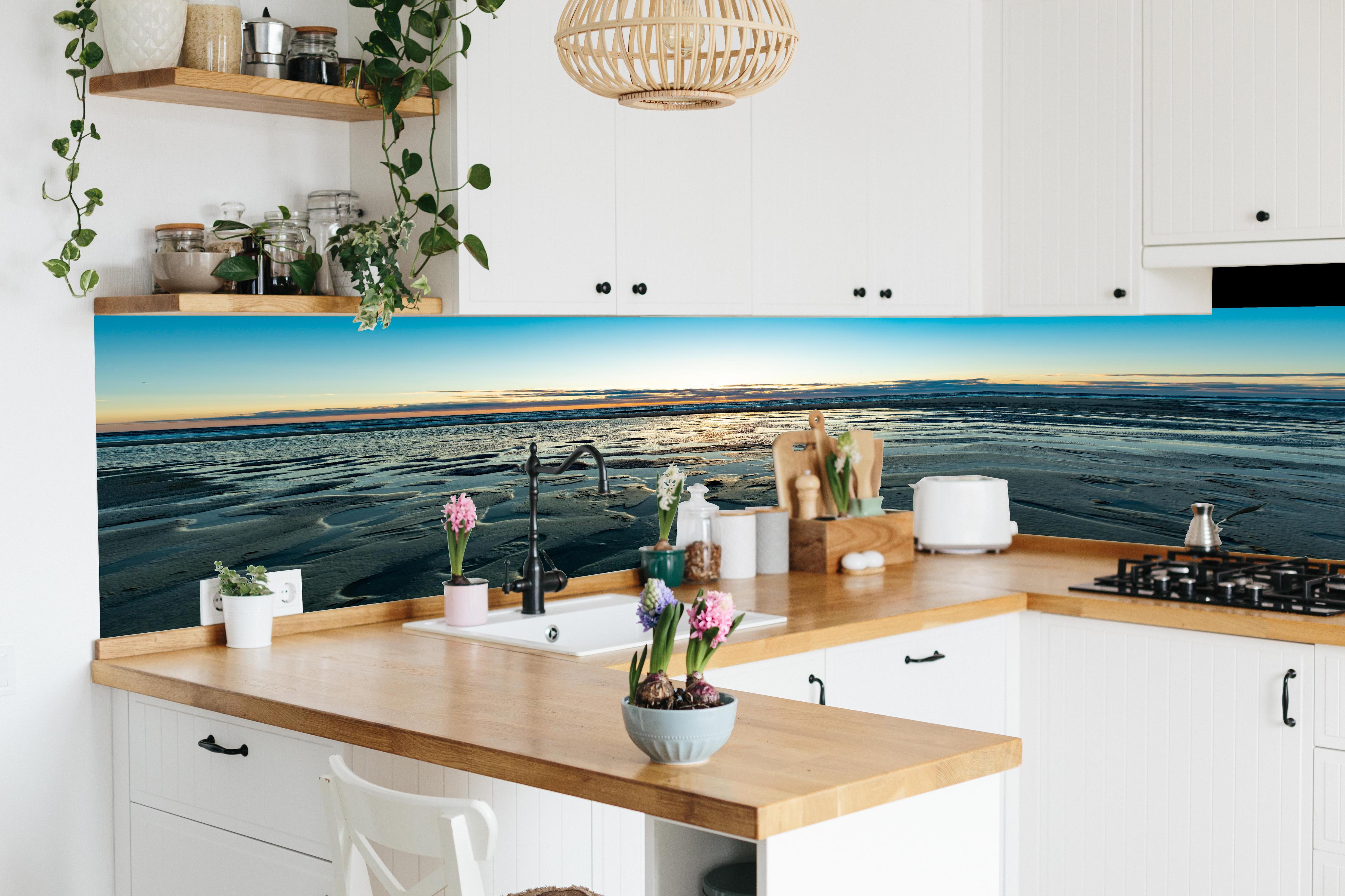 Küche - Wunderschöne blaue und orange Strandlandschaft mit Sonnenuntergang hinter weißen Hochglanz-Küchenregalen und schwarzem Wasserhahn